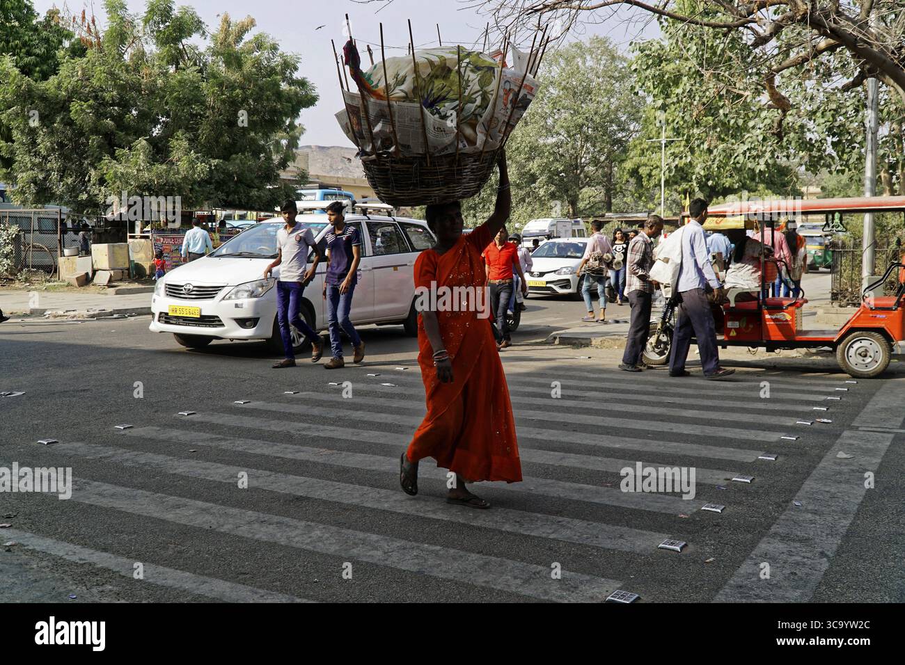Jaipur, Rajasthan, India settentrionale, India, Asia, una donna di colore arancione porta un cesto sulla testa e attraversa la strada Foto Stock