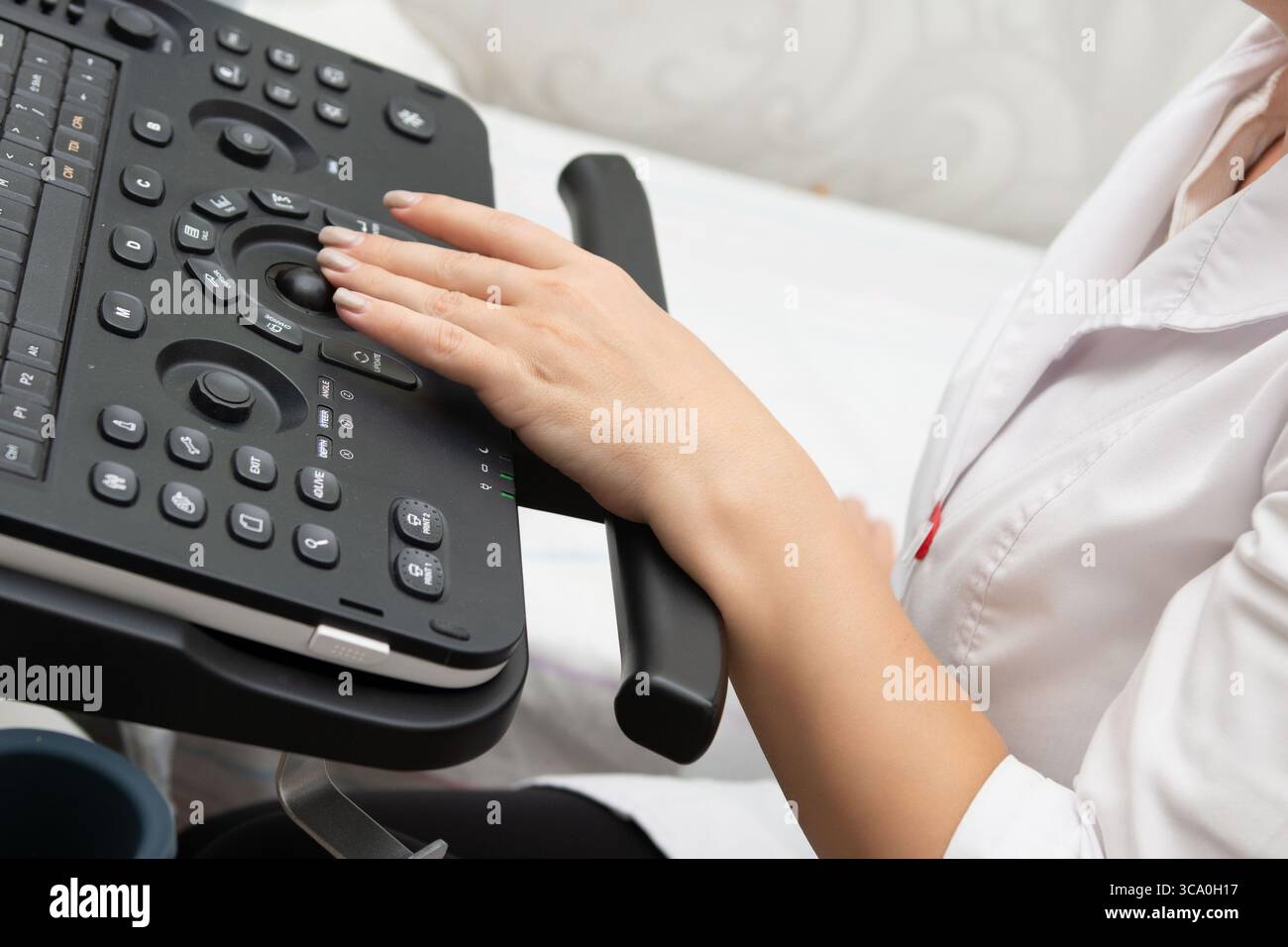 Questa immagine mostra la mano di un medico su una macchina a ultrasuoni, suggerendo un processo diagnostico preciso in un ambiente sanitario. Il dispositivo i Foto Stock