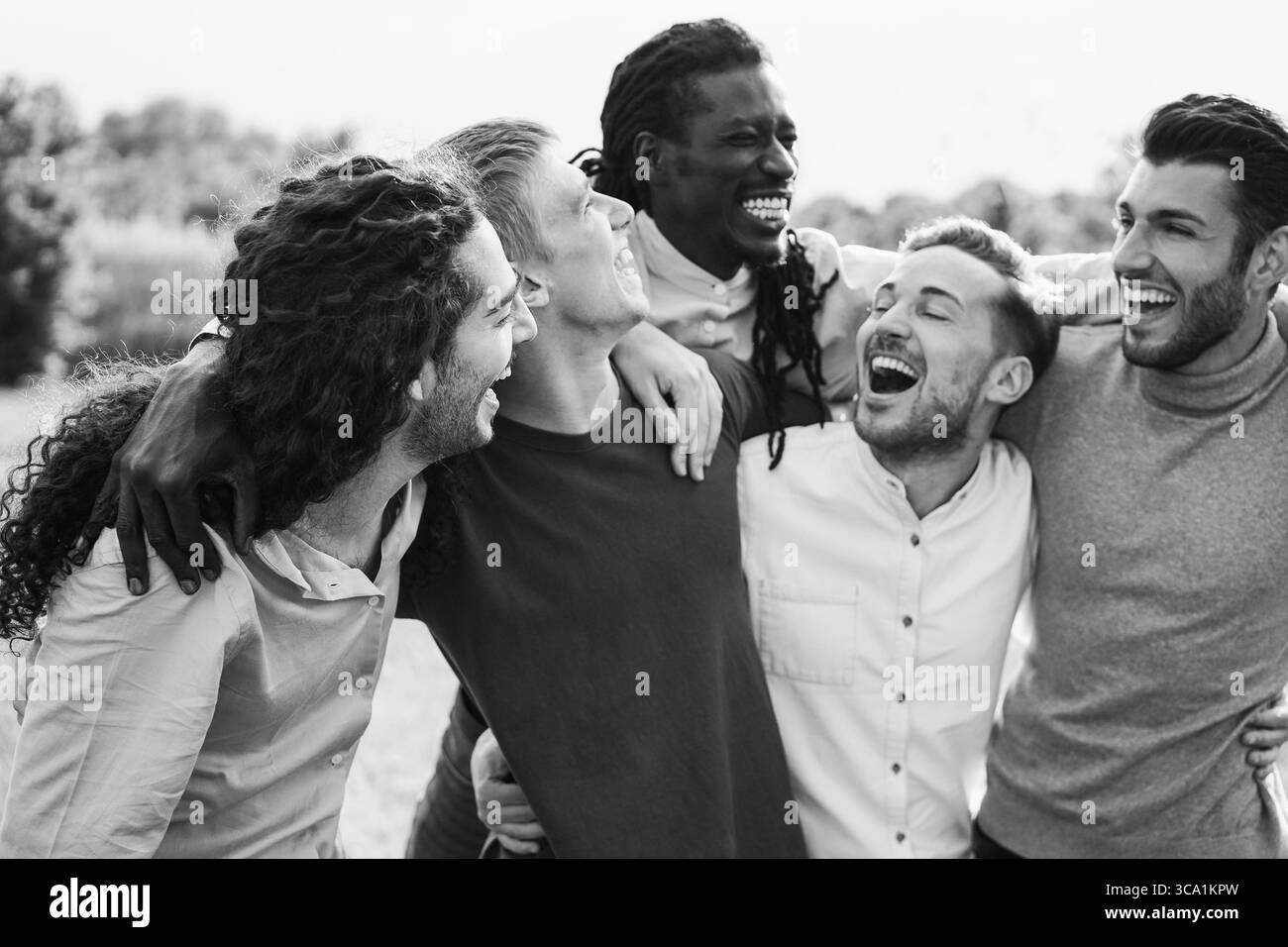Amici maschi felici che si divertono insieme all'aperto - gruppo di uomini multirazziali che si abbracciano a vicenda nel parco cittadino - concetto di amicizia e stile di vita Foto Stock