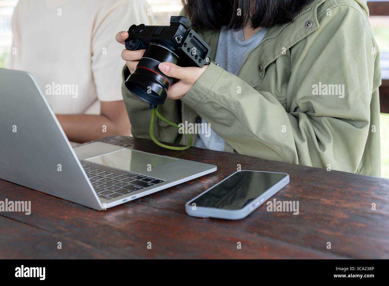 Una donna controlla le foto sulla sua fotocamera digitale con un laptop al suo fianco, lavorando o modificando le immagini. Foto Stock