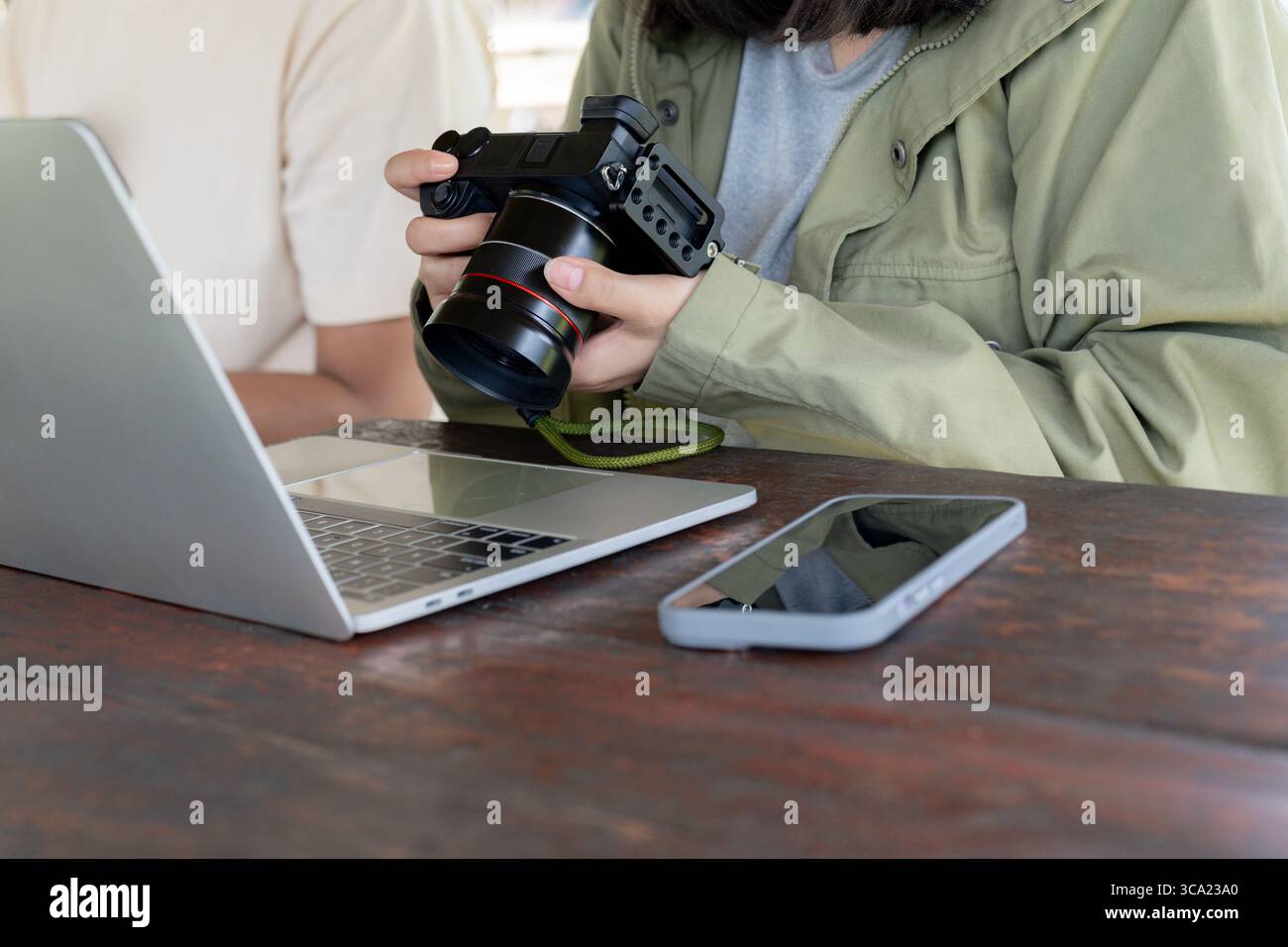Una donna controlla le foto sulla sua fotocamera digitale con un laptop al suo fianco, lavorando o modificando le immagini. Foto Stock