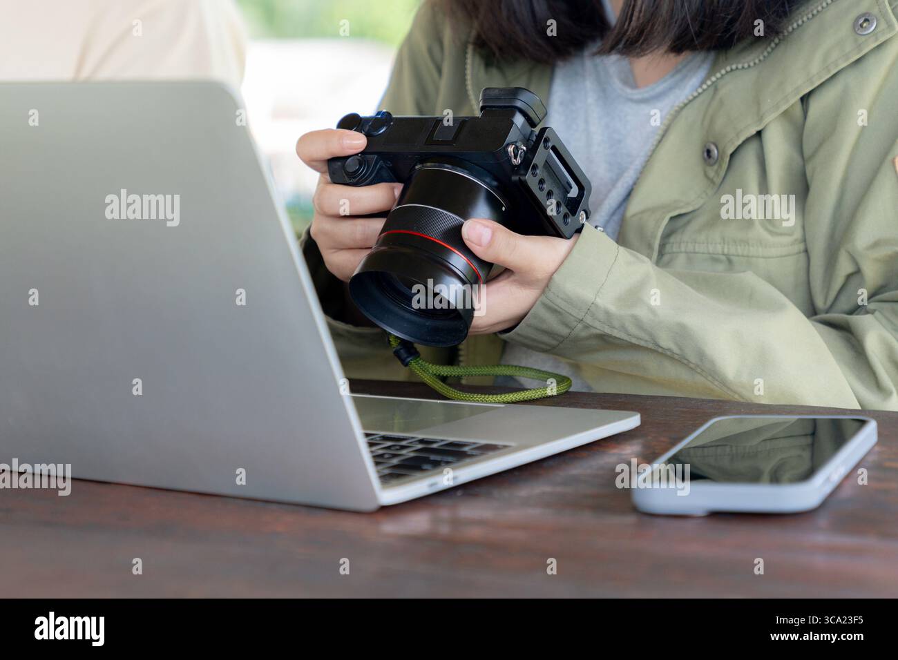 Una donna controlla le foto sulla sua fotocamera digitale con un laptop al suo fianco, lavorando o modificando le immagini. Foto Stock