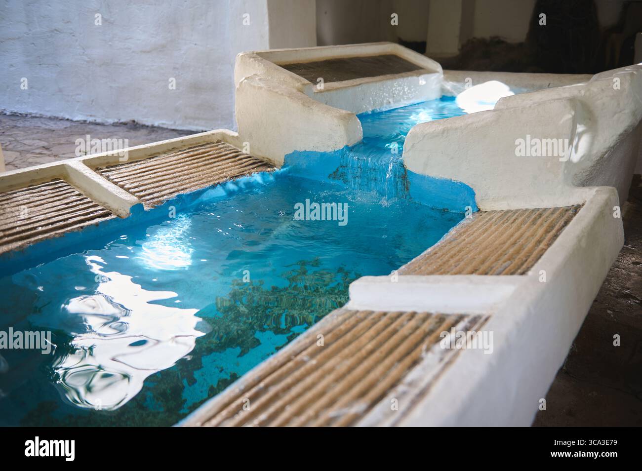 L'acqua azzurra fluisce attraverso un canale bianco strutturato con lati testurizzati, catturati in interni con un'atmosfera di luce naturale. La configurazione enfatizza se Foto Stock