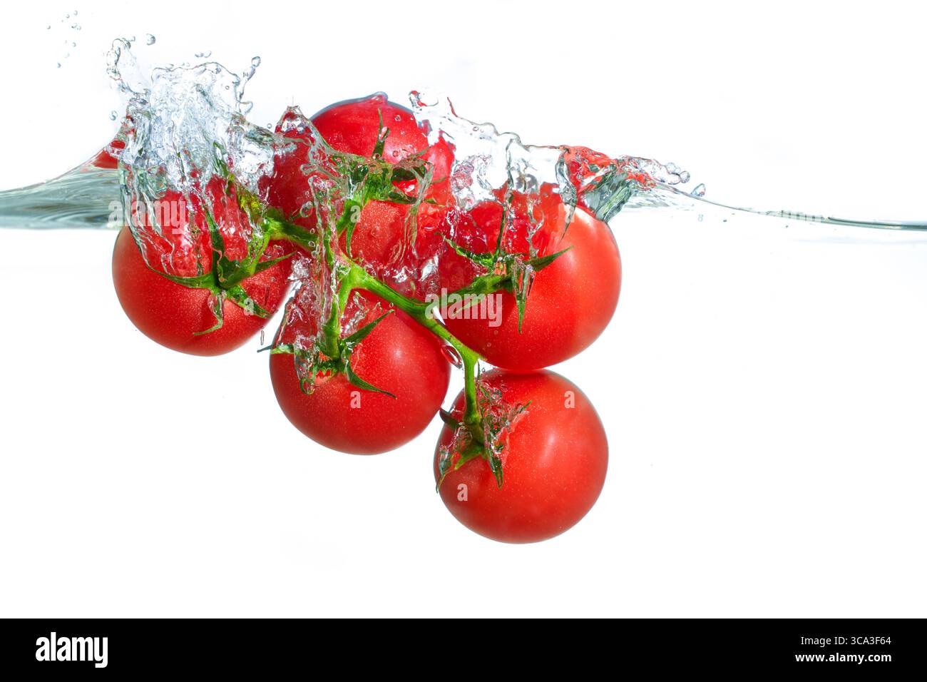 I pomodori ciliegini rossi vivaci creano spruzzi dinamici in acqua limpida, che mostrano freschezza e vitalità in un ambiente pulito e ben illuminato. Foto Stock