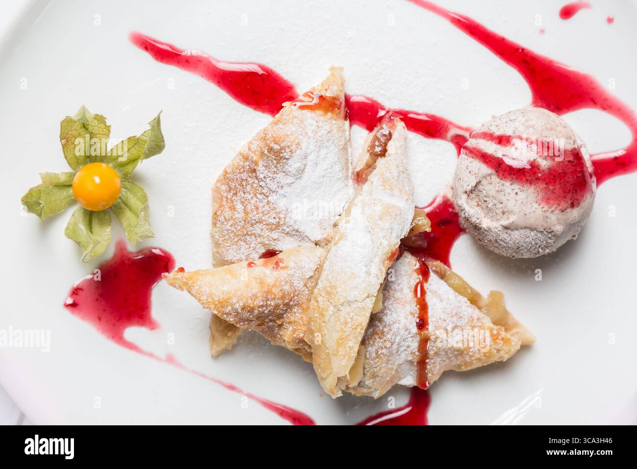 Strudel di mele con gelato, uva spina e frutta spalmata su piatto bianco. Foto Stock