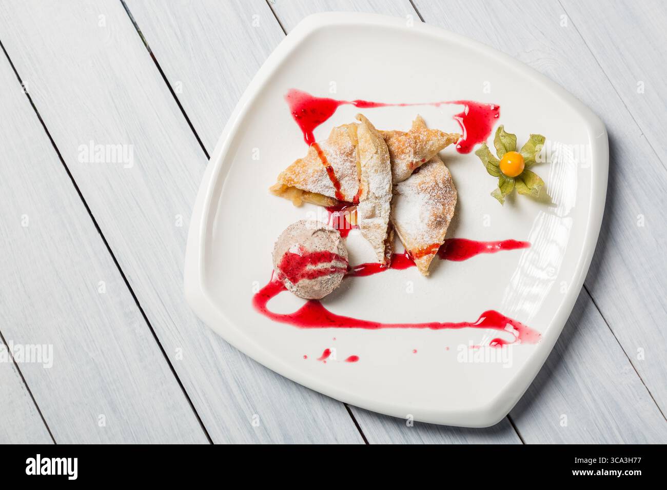 Strudel di mele con gelato, uva spina e frutta spalmata su piatto bianco. Vista dall'alto. Foto Stock