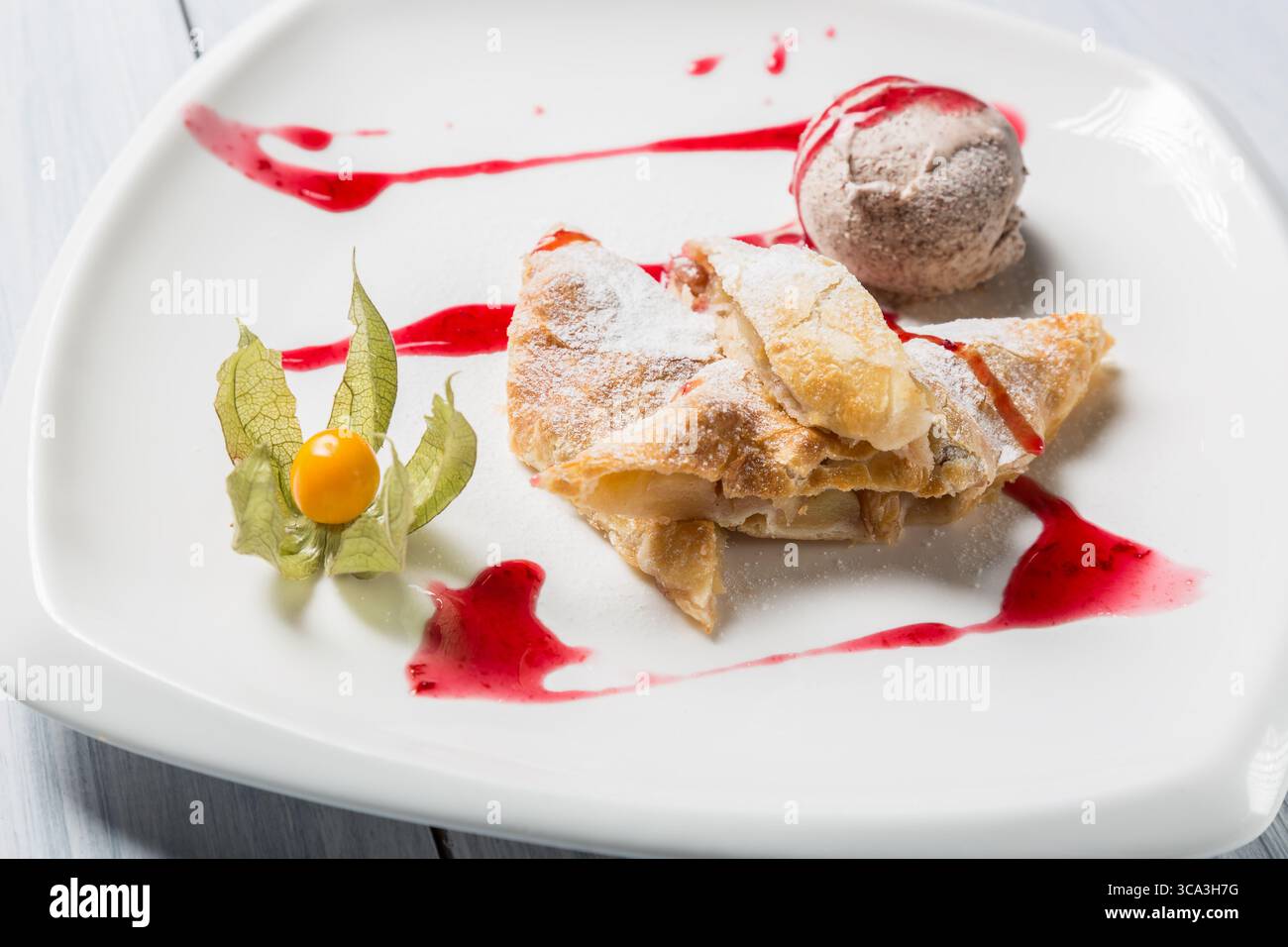 Strudel di mele con gelato, uva spina e frutta spalmata su piatto bianco. Foto Stock