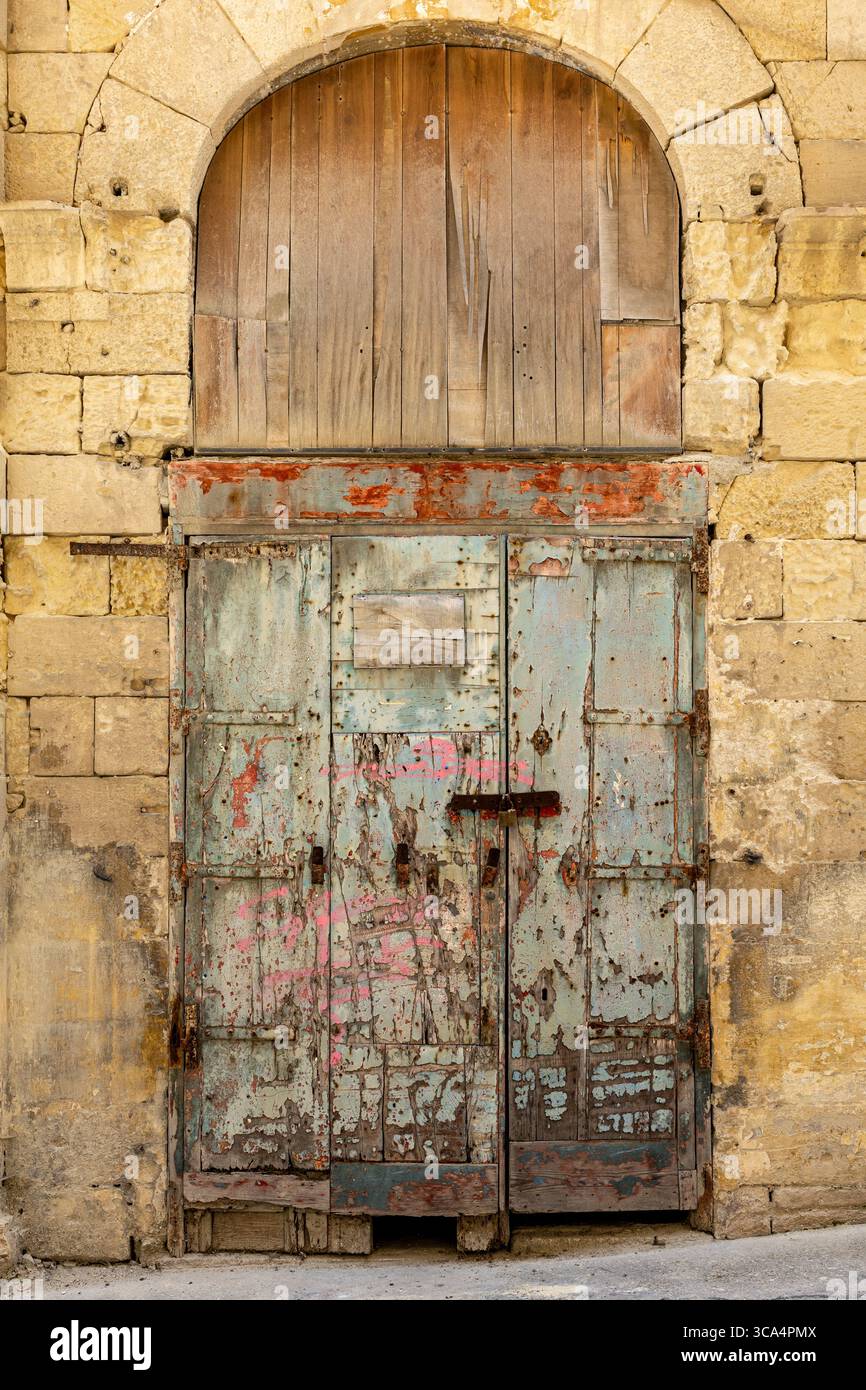 Antico ingresso con porte chiuse e pannelli in un tradizionale edificio di pietra calcarea. Forse ora in disuso. La Valletta, Malta. Foto Stock