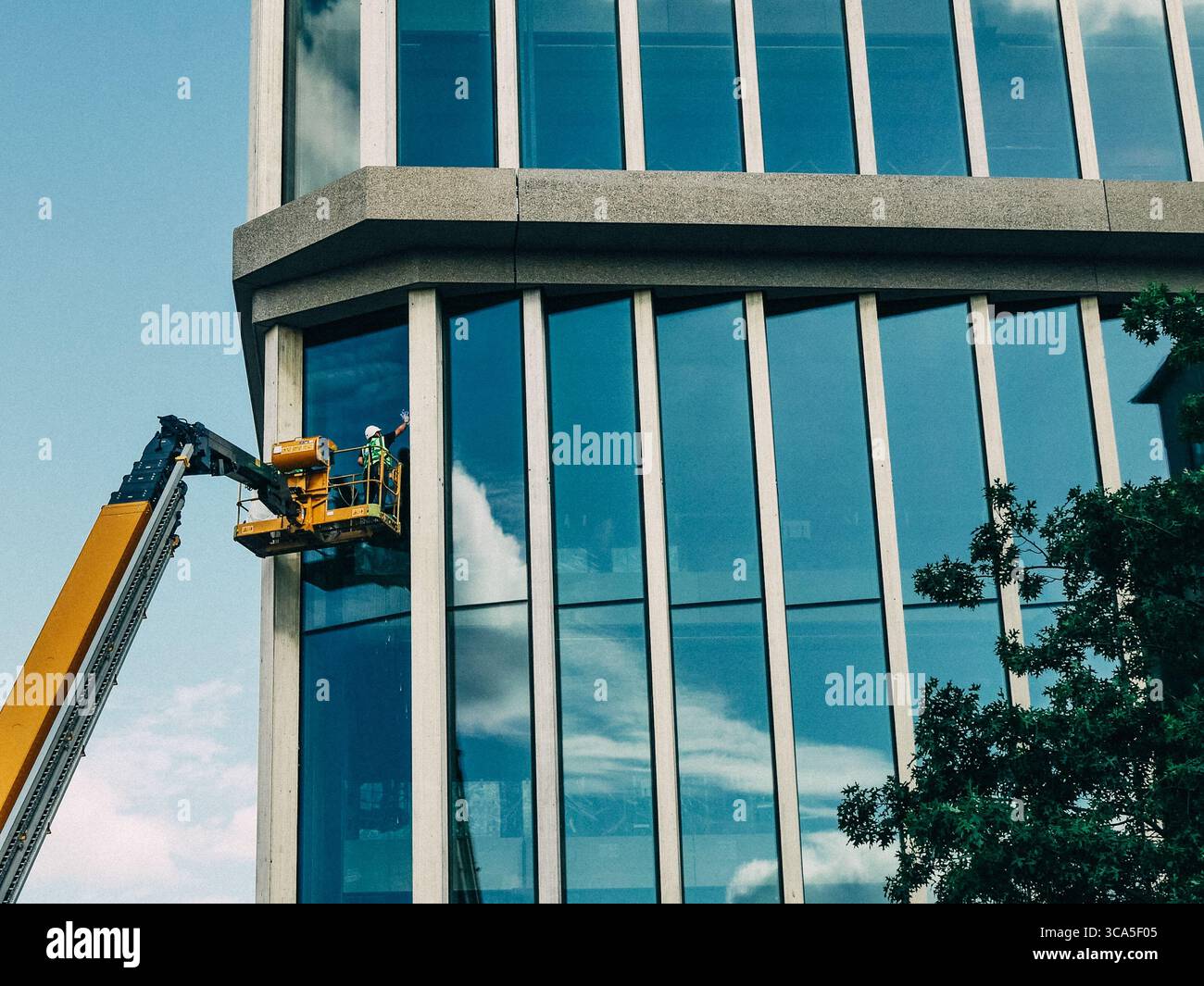 Lavoratore su una piattaforma sopraelevata che pulisce le finestre di vetro di un edificio aziendale Foto Stock