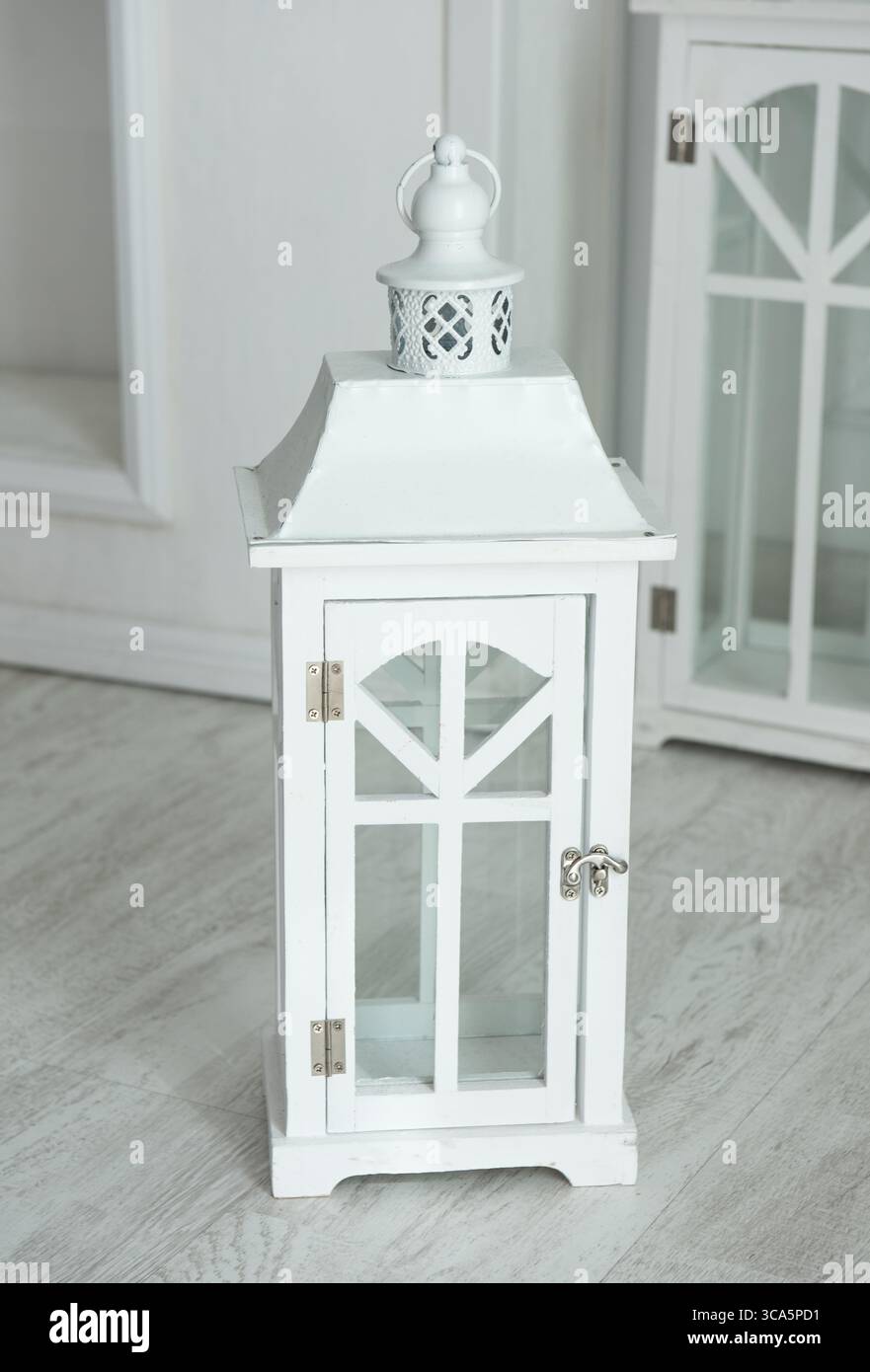 La lanterna bianca decorativa presenta pannelli in vetro e un design dettagliato della parte superiore, posizionata su un pavimento in legno chiaro, che aggiunge fascino agli spazi interni con ITS Foto Stock