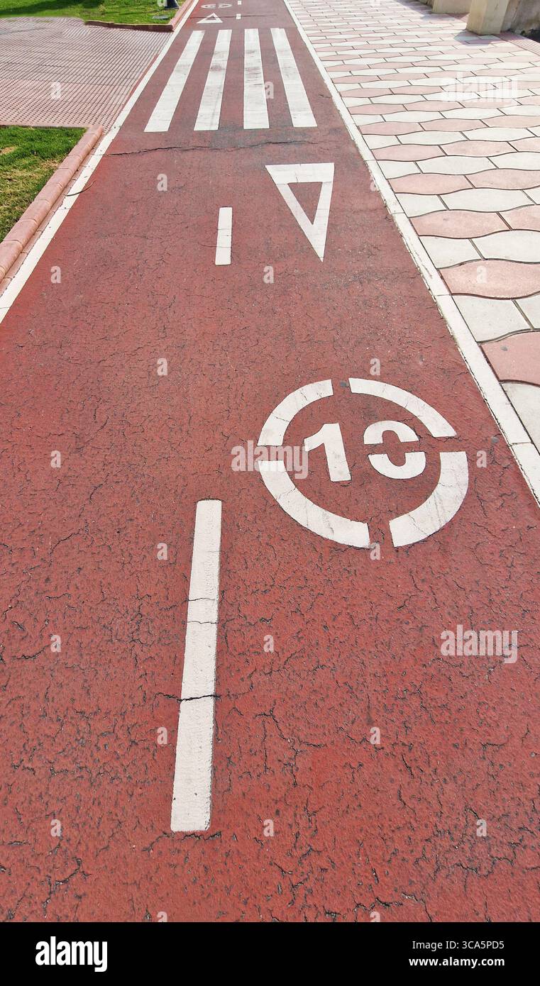 Almeria, Spagna - 25 maggio 2025: La pavimentazione rossa presenta frecce direzionali bianche e contrassegni del limite di velocità, che evidenziano il design urbano e la sicurezza per i pedoni Foto Stock