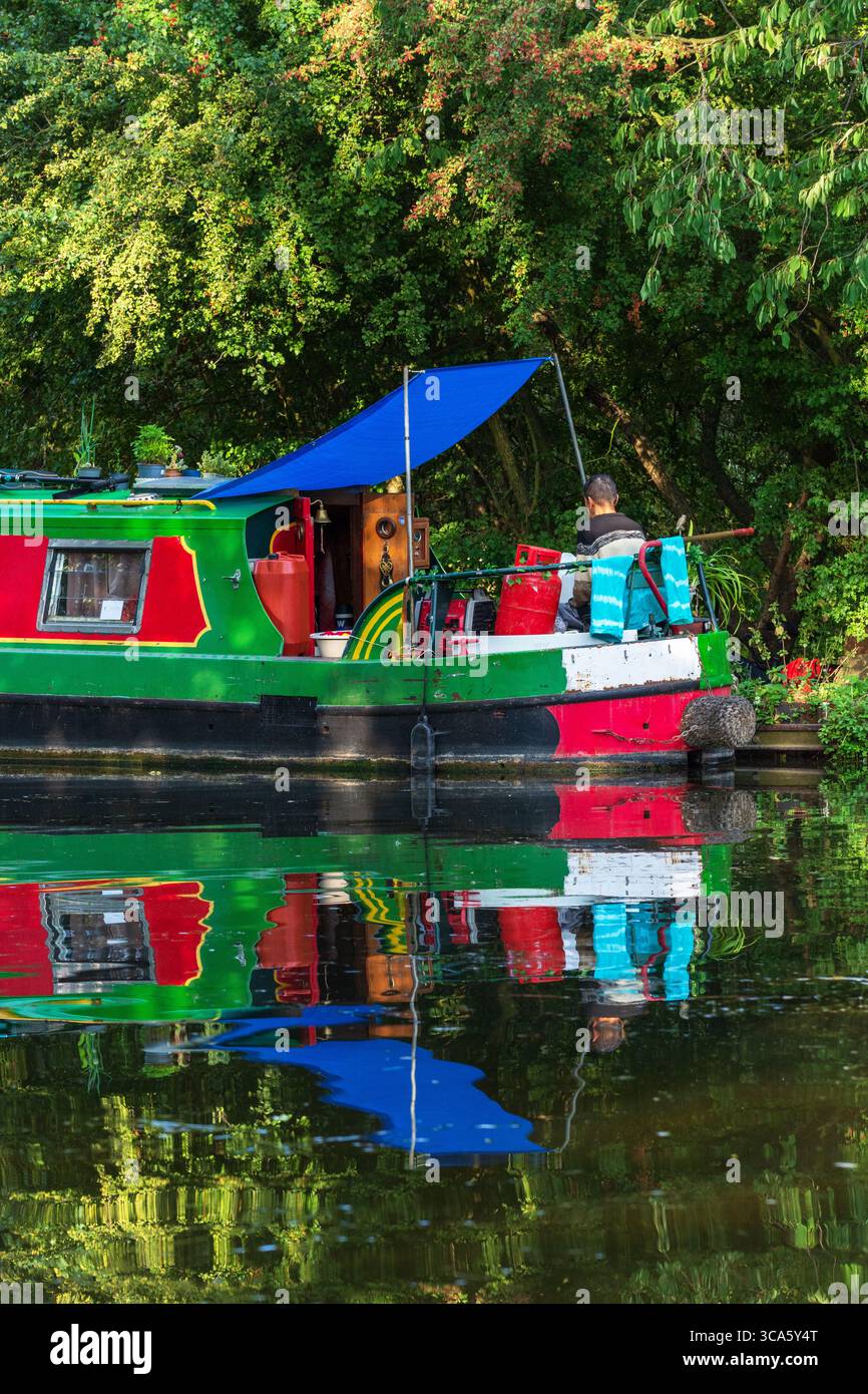 Un uomo seduto su un motoscafo che legge in estate, Lee Navigation, Lea Valley Canal, Londra, Inghilterra, REGNO UNITO. Stili di vita alternativi a Londra. Foto Stock
