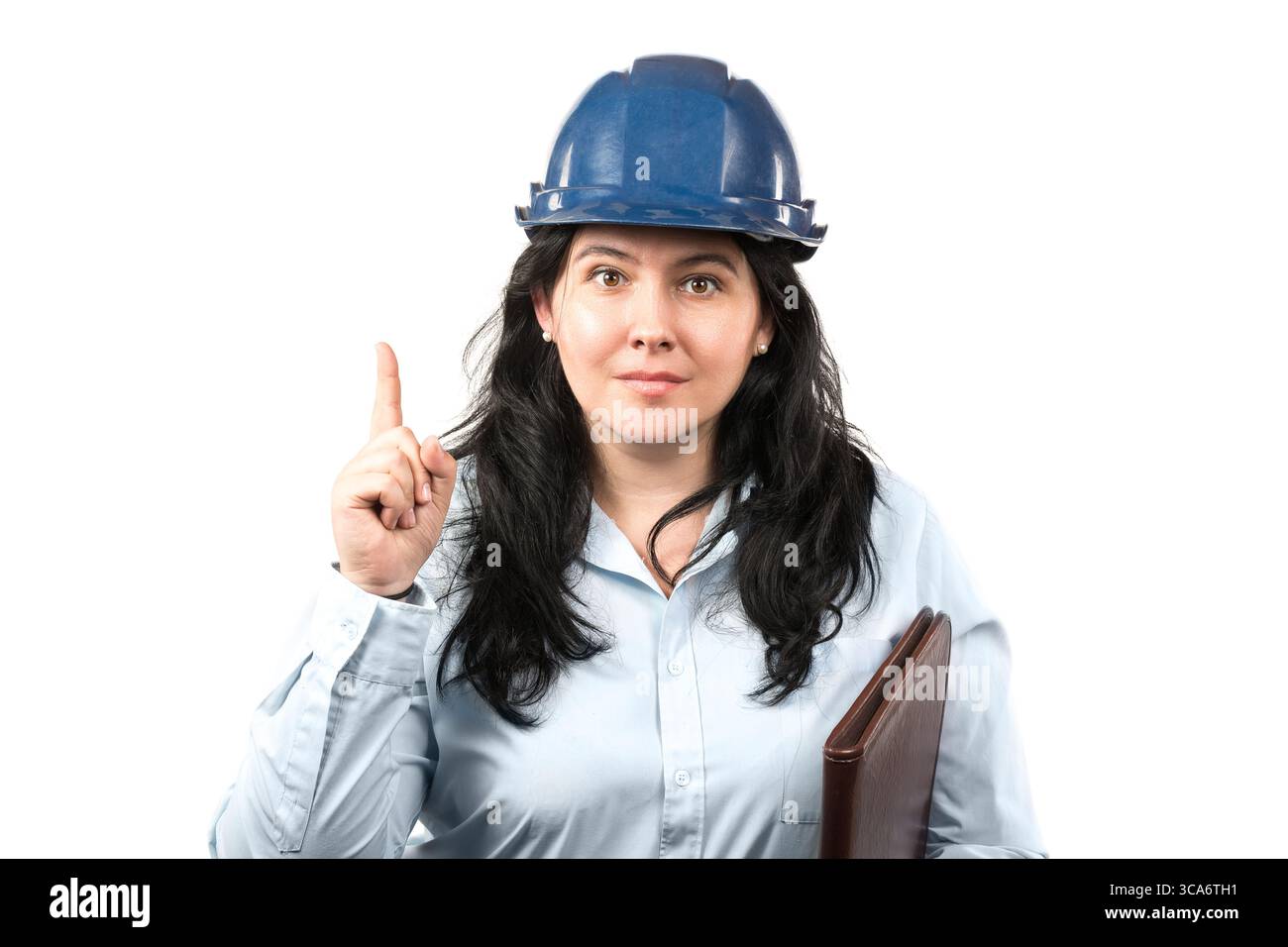 Giovane e attraente donna bruna ingegnere o architetto con cappello di sicurezza blu che mostra il dito del puntatore isolato su sfondo bianco. Foto Stock