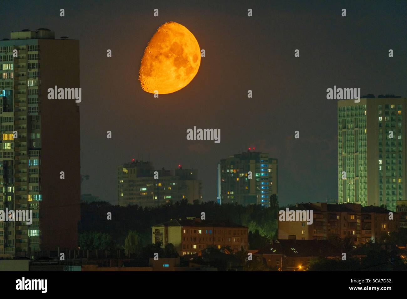 Luna arancione luminosa che si innalza sullo skyline della città di Kiev di notte. Foto Stock