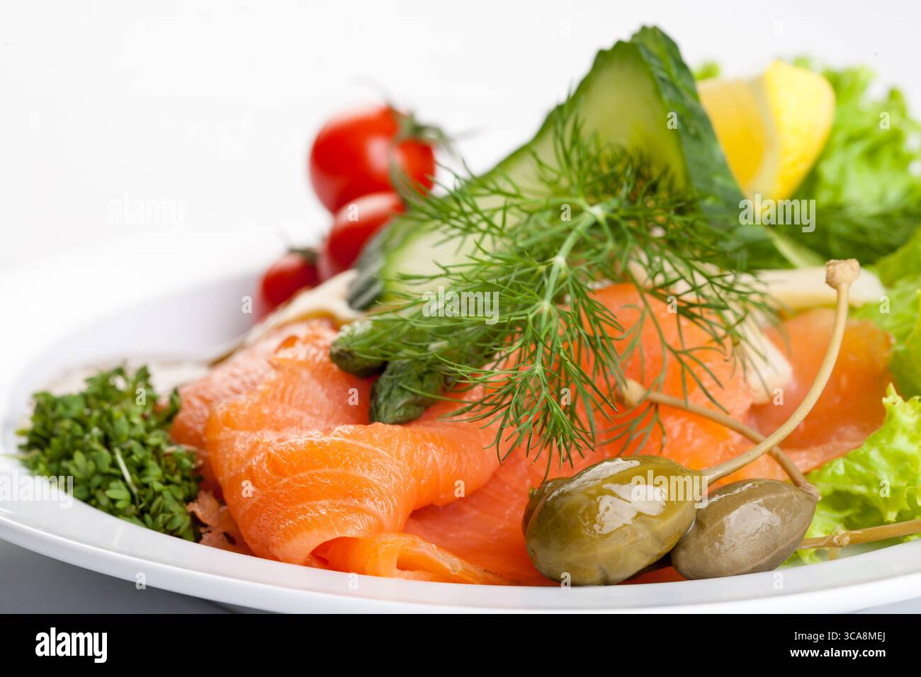piatto salutare di salmone affumicato con cetriolo, pomodori, salsa ed erbe fresche su un piatto bianco, una foto da studio di un pasto gourmet Foto Stock