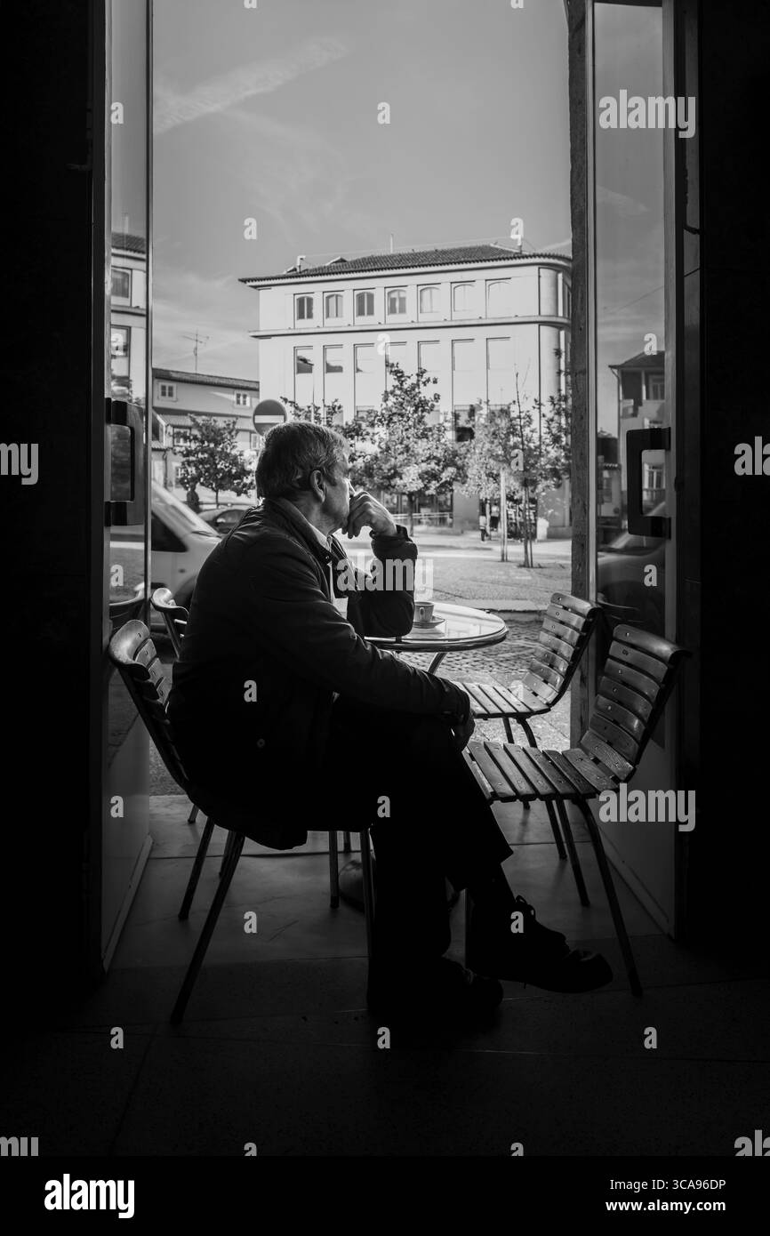 Uomo anziano che gusta un caffè al tradizionale Cafe Window portoghese a Guimaraes, contemplativo, stile di vita, cultura portoghese, rituale del caffè mattutino Foto Stock