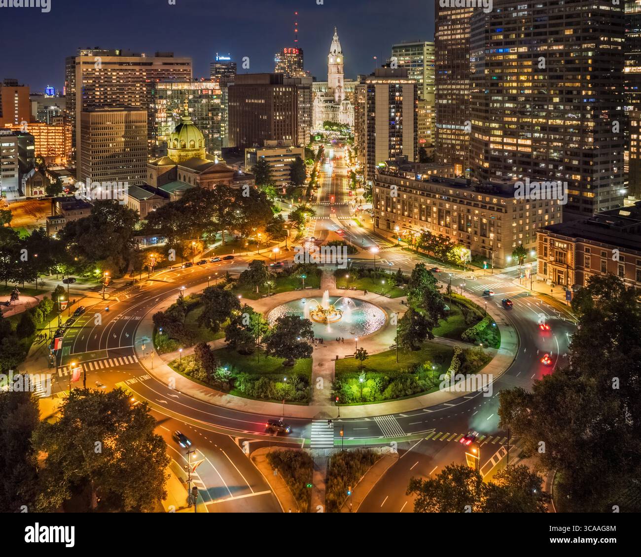 Un vibrante paesaggio urbano notturno mette in mostra un'area urbana ben illuminata con una prominente piazza circolare e una fontana conosciuta come Logan Square a Philadelphia, Pen Foto Stock
