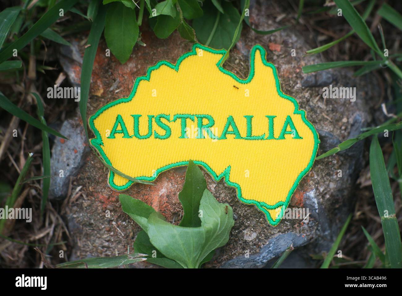 Eco patch con mappa dell'Australia, cucita con tessuto e filo, posta su un sentiero nella foresta. Circondato dalla natura, dalla luce del sole e dal verde. Foto Stock