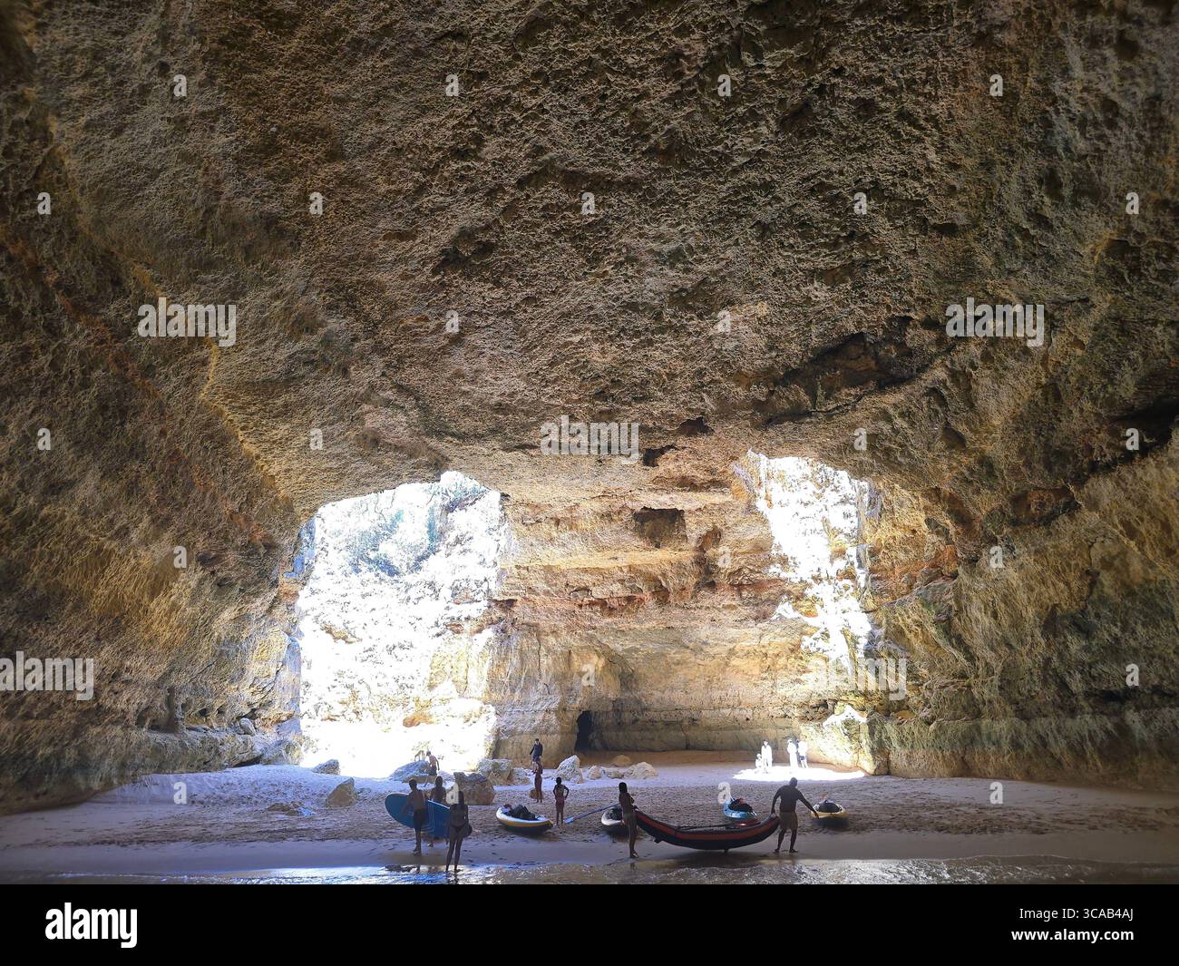 Turisti con kayak all'interno della famosa grotta Benagil in Algarve, Portogallo, con la luce del sole che scorre attraverso le grandi aperture naturali nelle pareti della grotta Foto Stock