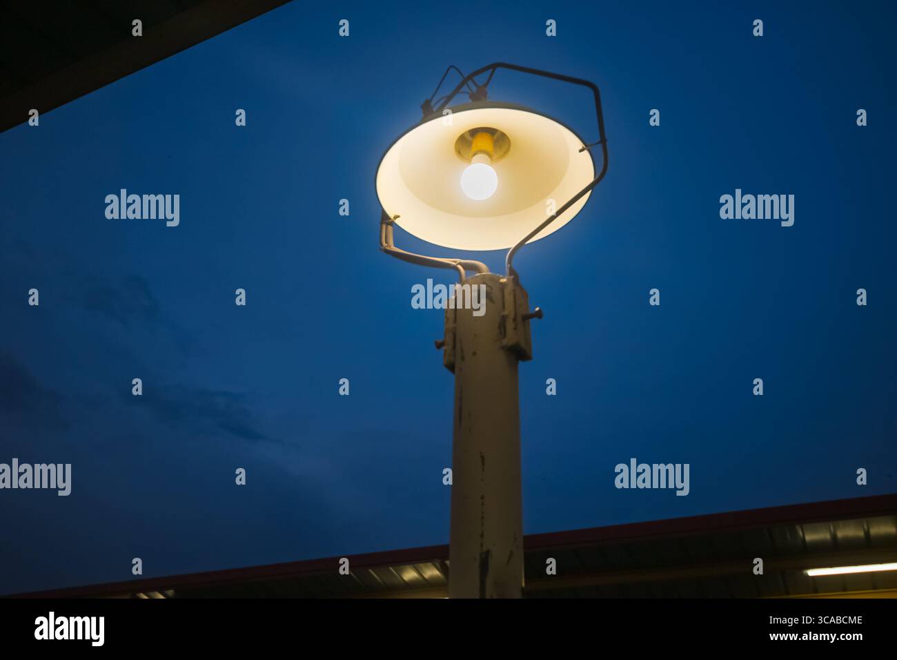Lampada in ferro d'epoca che si illumina dolcemente contro il cielo notturno, unendo stile retrò e illuminazione funzionale. Foto Stock