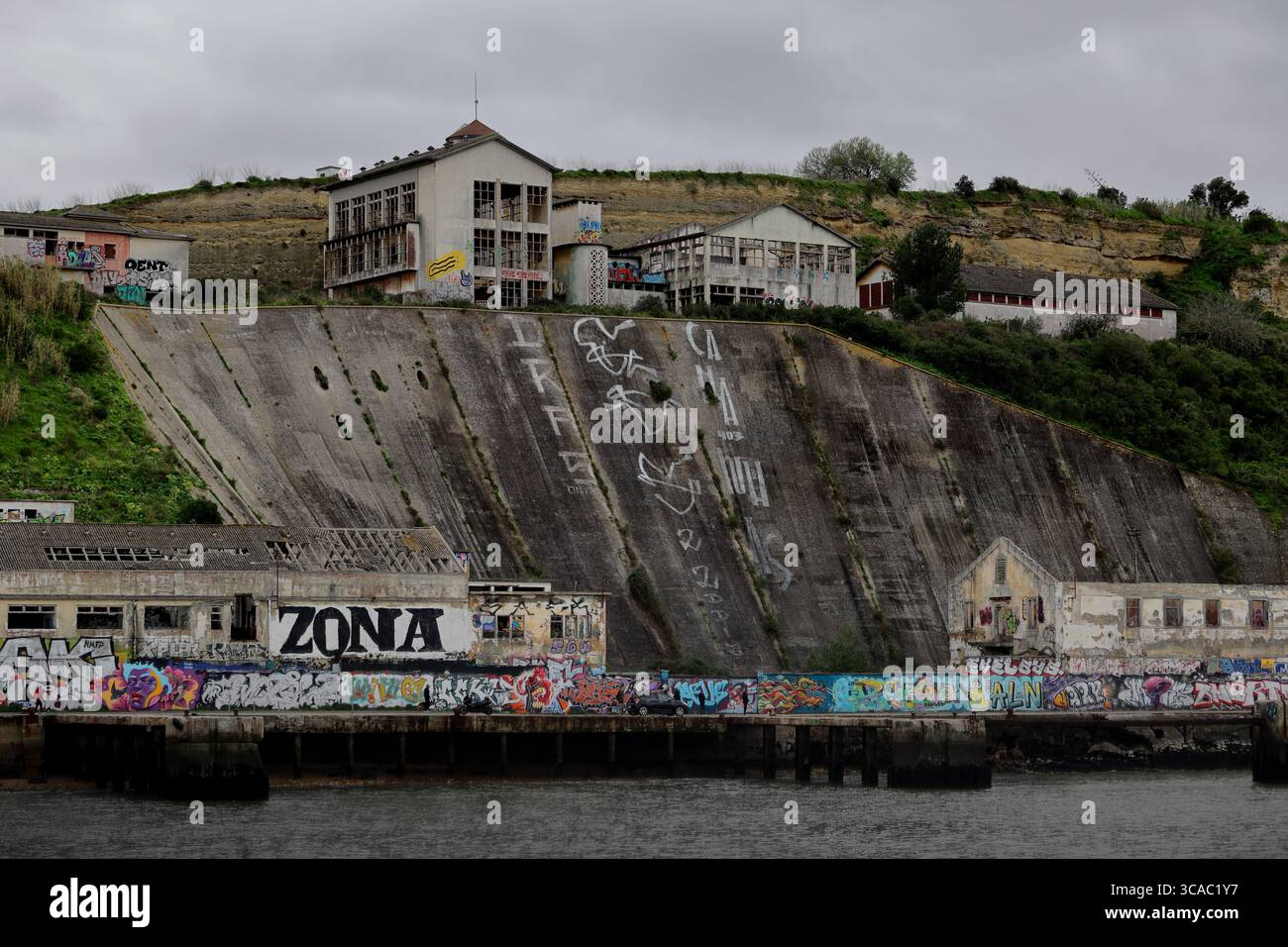 Gli edifici ricoperti di graffiti si ergono sopra un ripido argine a Praia das Lavadeiras ad Almada, Lisbona, mescolando arte urbana con un suggestivo paesaggio costiero. Foto Stock