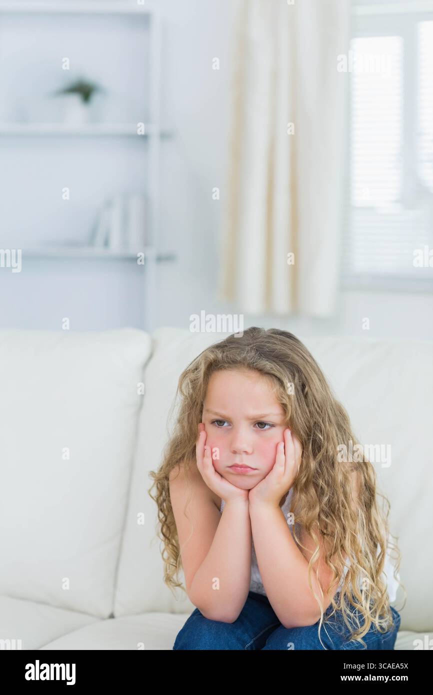 Bambino che poggia il mento sulle mani sul divano in pelle bianca a casa accanto all'unità scaffalatura Foto Stock