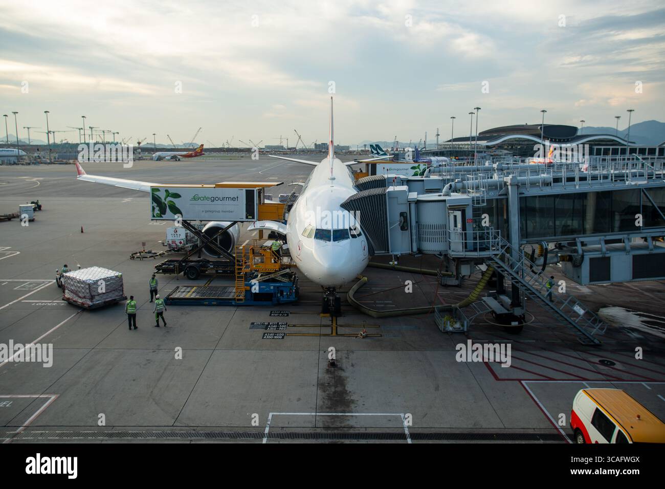 Un aereo è attraccato al cancello dell'aeroporto, collegato al ponte dei jet, mentre l'equipaggio di terra carica il carico e la ristorazione prima della partenza. Foto Stock