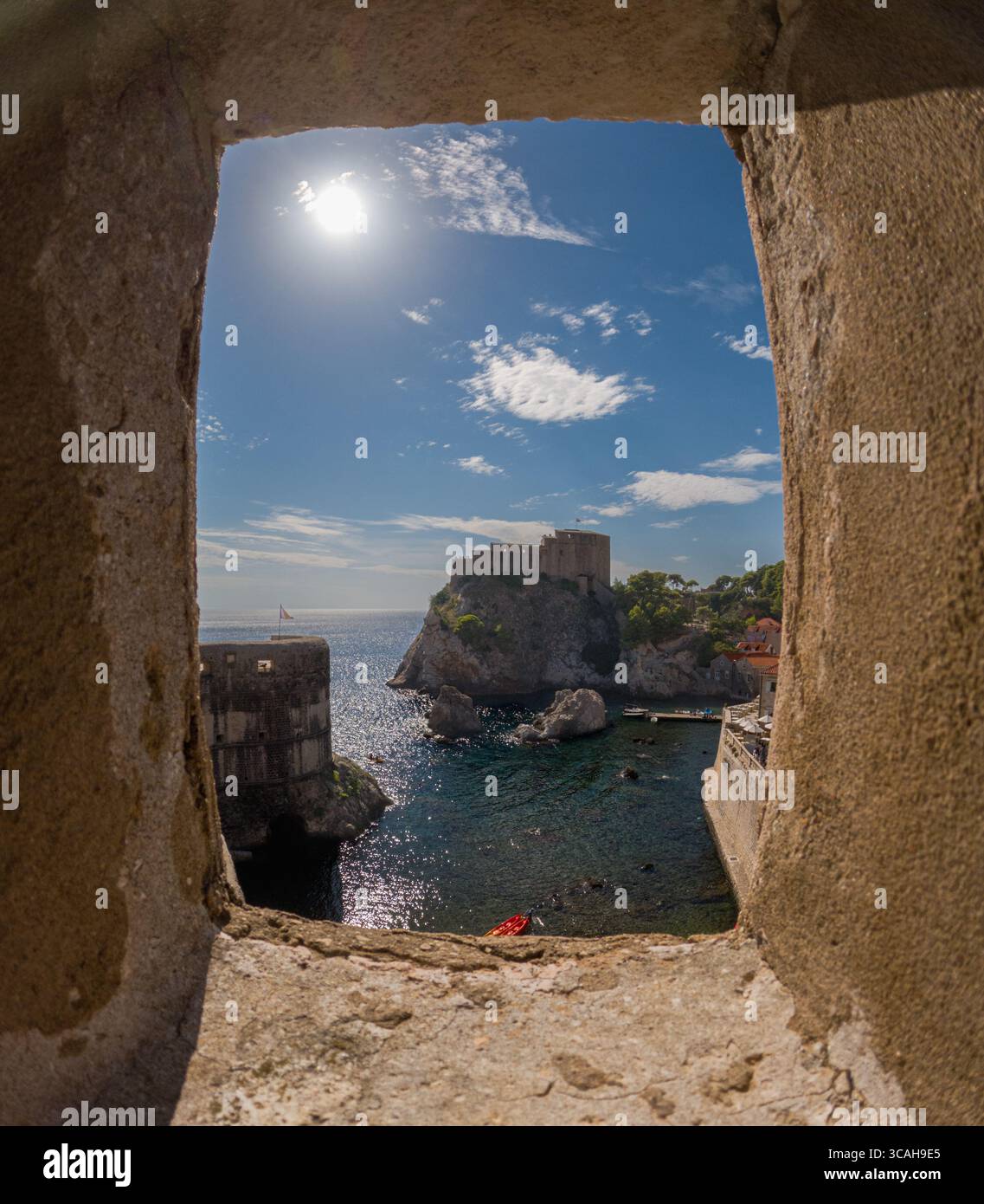 Dubrovnik, Croazia - 14 settembre 2023: Una vista di Fort Lovrijenac attraverso una finestra in pietra. I turisti fanno kayak nell'acqua sotto il forte, godendosi la S Foto Stock