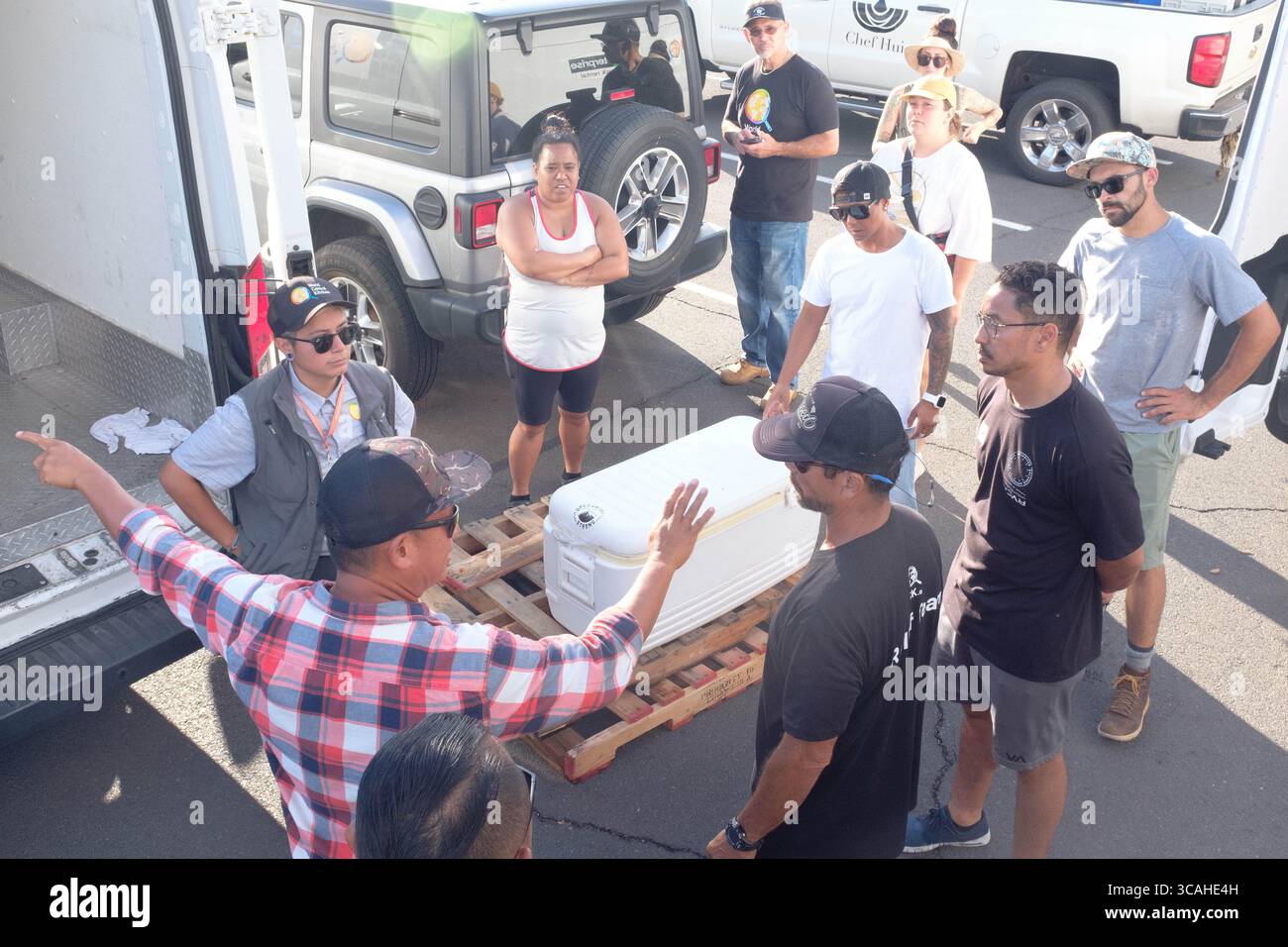12 agosto 2023, Lahaina, Hawaii, USA: Lo chef ISAAC BANCACO (a sinistra, in camicia a quadri), Executive Chef del Pacific'o a Lahaina, distrutto dall'incendio, dirige i volontari dello Chef Hui nei loro incarichi di distribuzione a Lahaina. Lo chef Bancaco ha perso il suo ristorante, la sua casa, e tutto quello che possedeva, tranne per i vestiti sulle spalle nel fuoco. Ha organizzato e cucinato con lo Chef Hui a partire dal giorno dopo l'incendio in vestiti presi in prestito da un amico. Questo è tipico della risposta di coloro che sono in grado, al di fuori dei canali ufficiali. Con GREG SHEPHERD e KELII HEEN e un abile Foto Stock