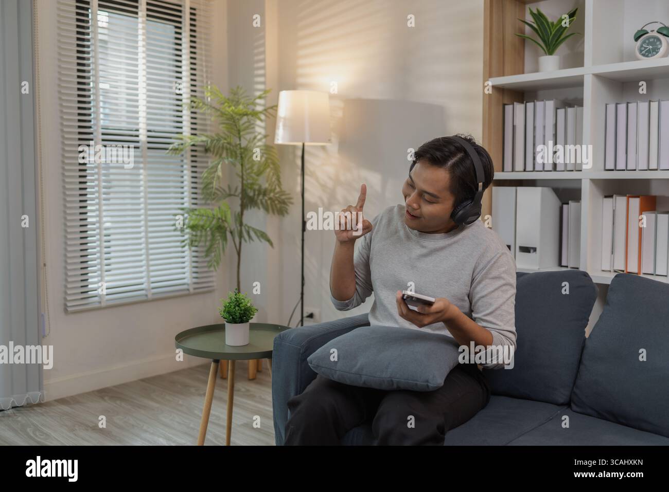 Un giovane uomo si rilassa a casa, godendo del tempo libero sul divano. Sta ascoltando musica con le cuffie, guardando film e cantando, expressi Foto Stock