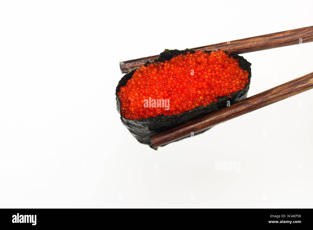 Primo piano di un singolo sushi gunkan maki perfettamente realizzato, con riso, nori e tobiko (uova di pesce volante), tenuto delicatamente da bacchette. Foto Stock