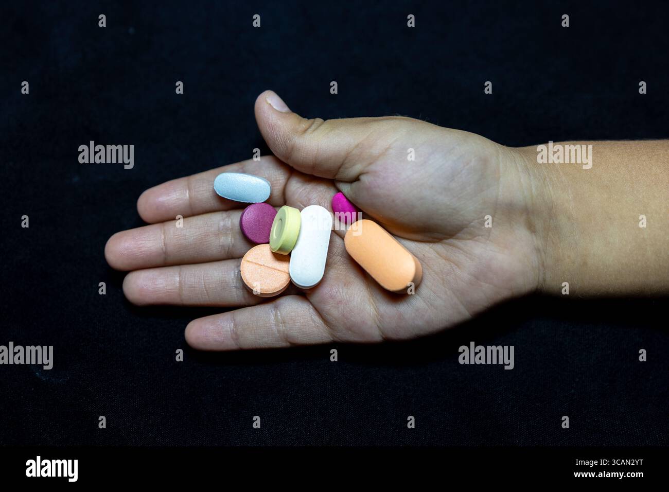 palmo per bambini pieno di colorate compresse mediche su sfondo scuro Foto Stock
