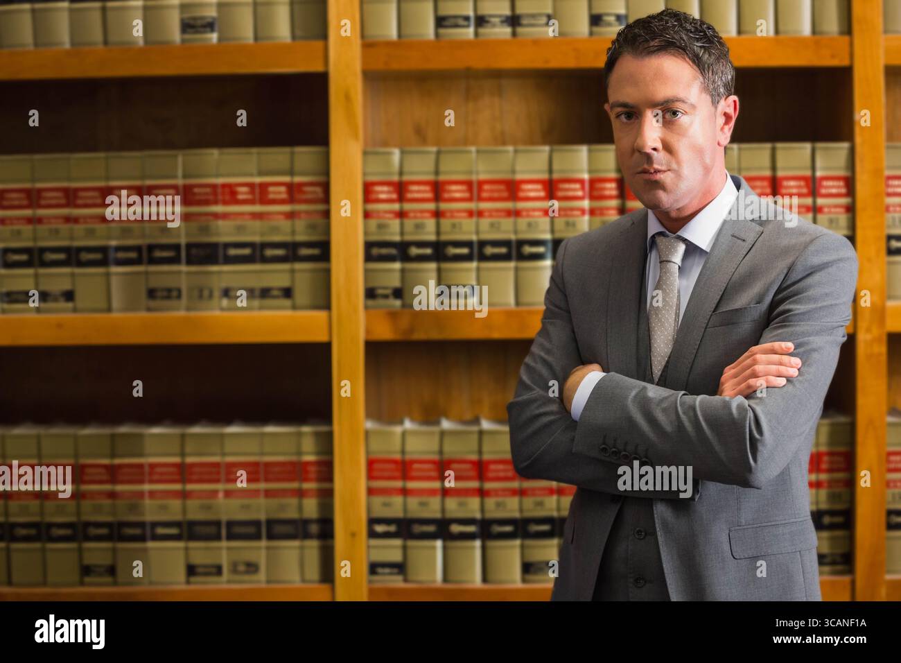 Uomo in piedi con le braccia incrociate in tuta grigia e cravatta alle librerie della biblioteca legale, spazio copia Foto Stock