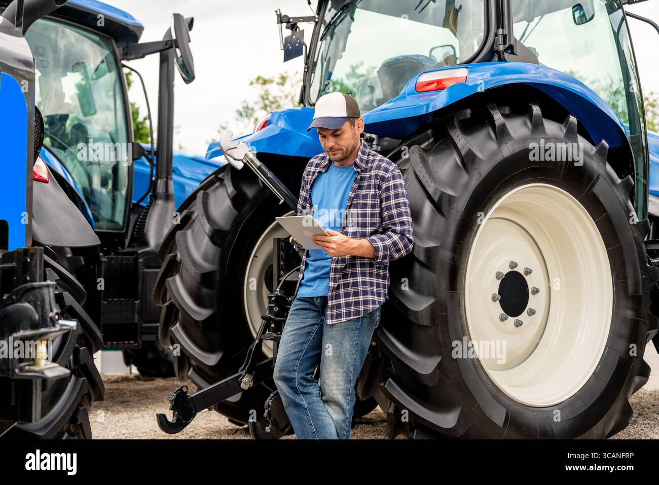 Agricoltore maschio che utilizza un tablet digitale vicino ai trattori agricoli Foto Stock
