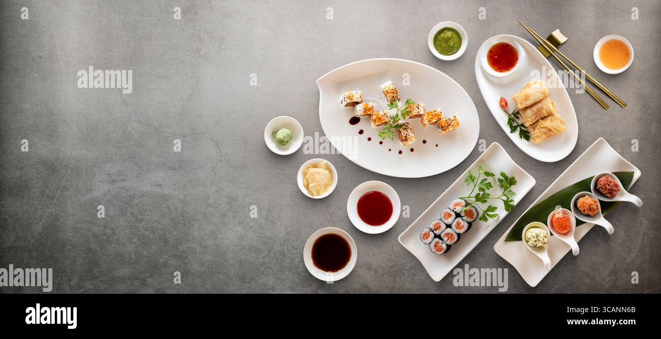I sushi Rolls variano con riso, pesce e salse su fondo in pietra. Vista superiore con spazio di copia. Foto Stock