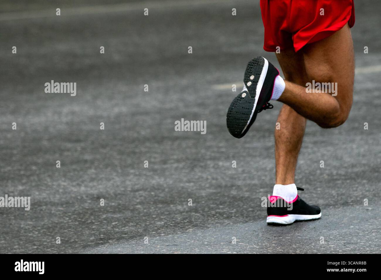 maratona di corsa su asfalto grigio bagnato con le gambe dei corridori in primo piano Foto Stock