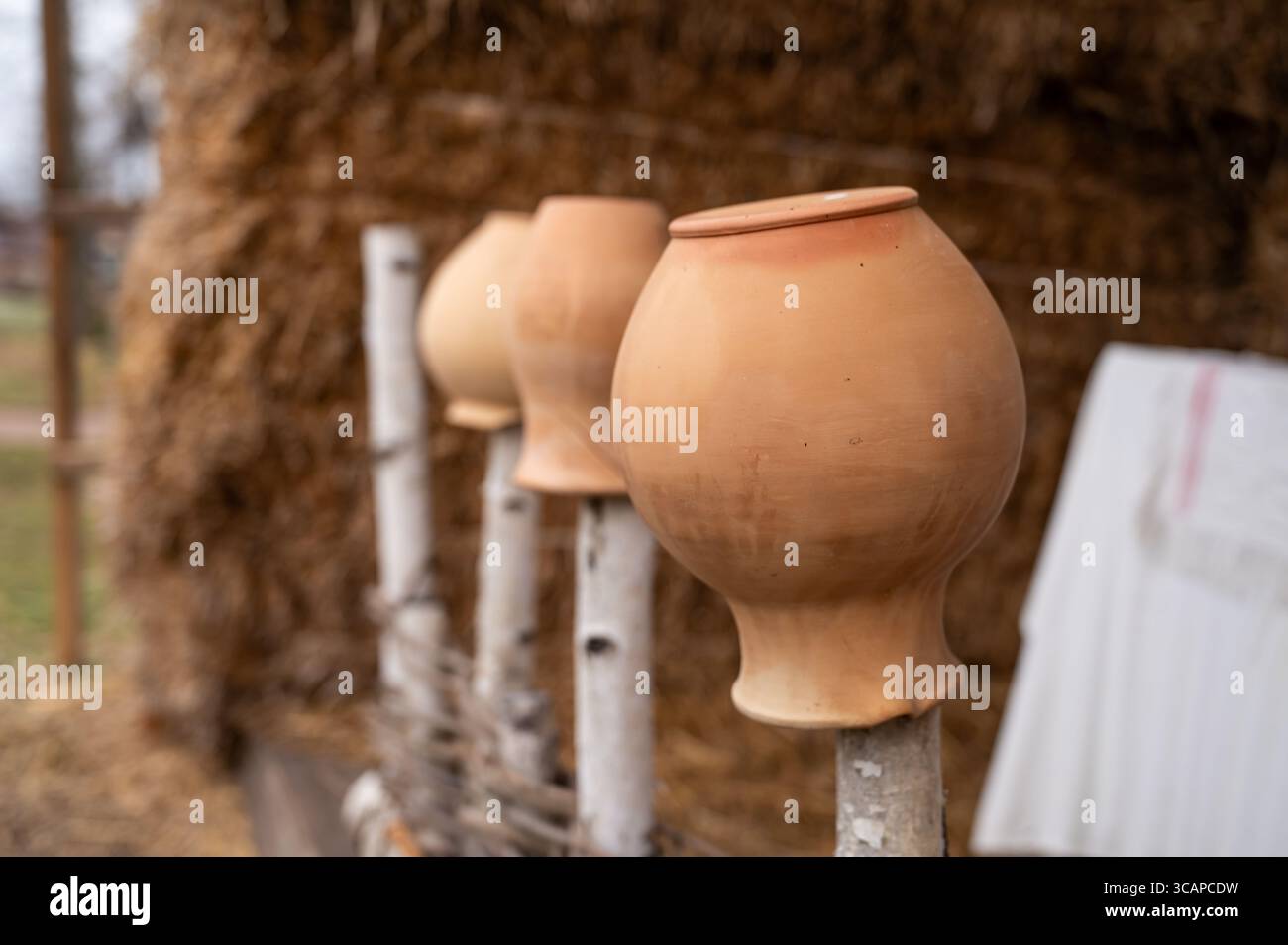 antiche caraffe rustiche di argilla poste sul collo su una recinzione di legno, sullo sfondo di un pagliaio, un elemento della vita di un antico villaggio Foto Stock