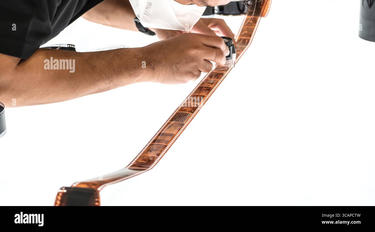 Un uomo che esamina da vicino una striscia di pellicola a colori sviluppata sotto ingrandimento su uno sfondo bianco. Foto Stock