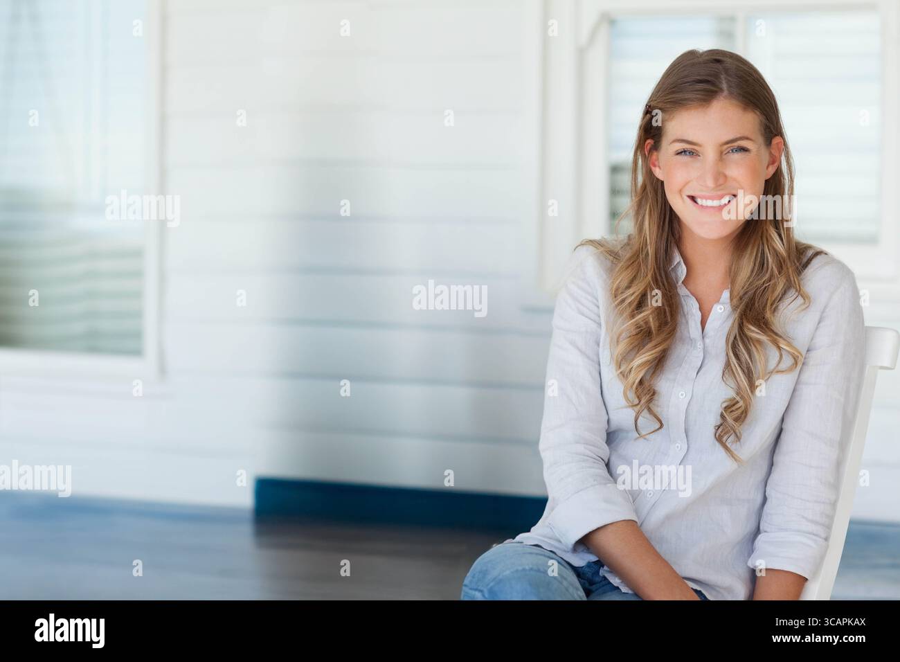 Donna seduta su una sedia bianca sul portico sorridente alla macchina fotografica con sfondo in legno e spazio per le copie Foto Stock
