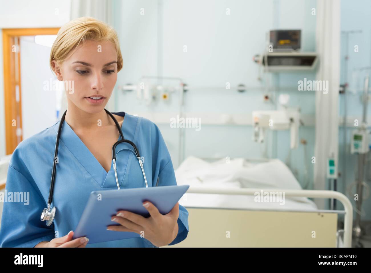 Medico donna che esamina i dati del paziente su tablet dal letto di ospedale con stetoscopio Foto Stock