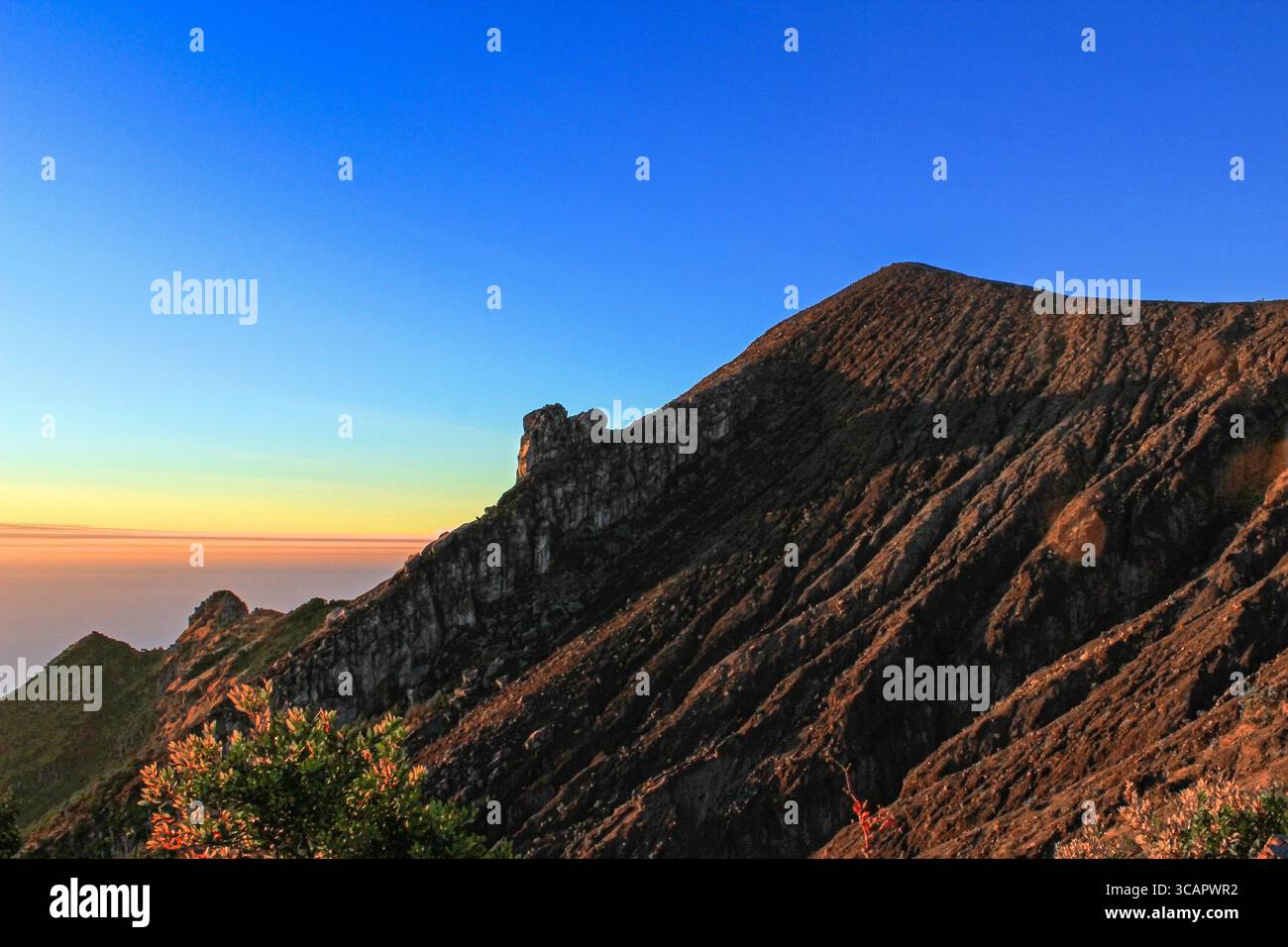 Una spettacolare cresta di montagna all'alba con superfici rocciose affilate e un cielo radioso che passa dal blu intenso alle calde tonalità dorate. Foto Stock