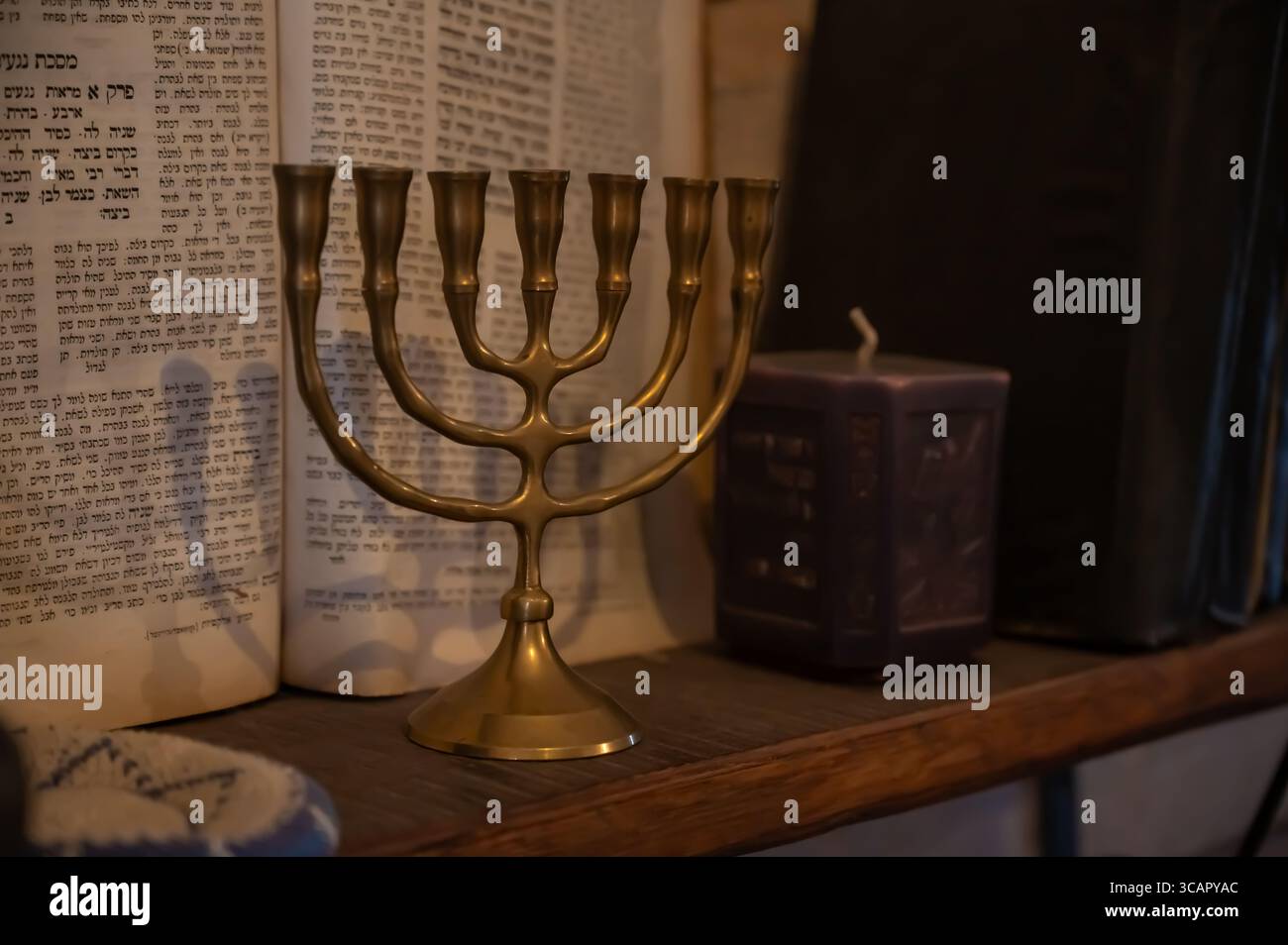 Una menorah in ottone si erge su una piattaforma di legno sullo sfondo di testi ebraici, che simboleggiano l'eredità e la tradizione ebraiche. Nelle vicinanze c'è una candela decorativa Foto Stock