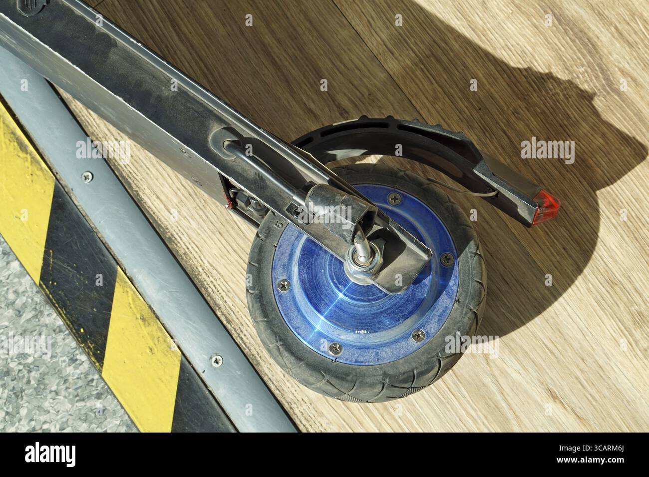 Ruota rotto di un piccolo e moderno scooter elettrico sullo sfondo di un pavimento in legno Foto Stock