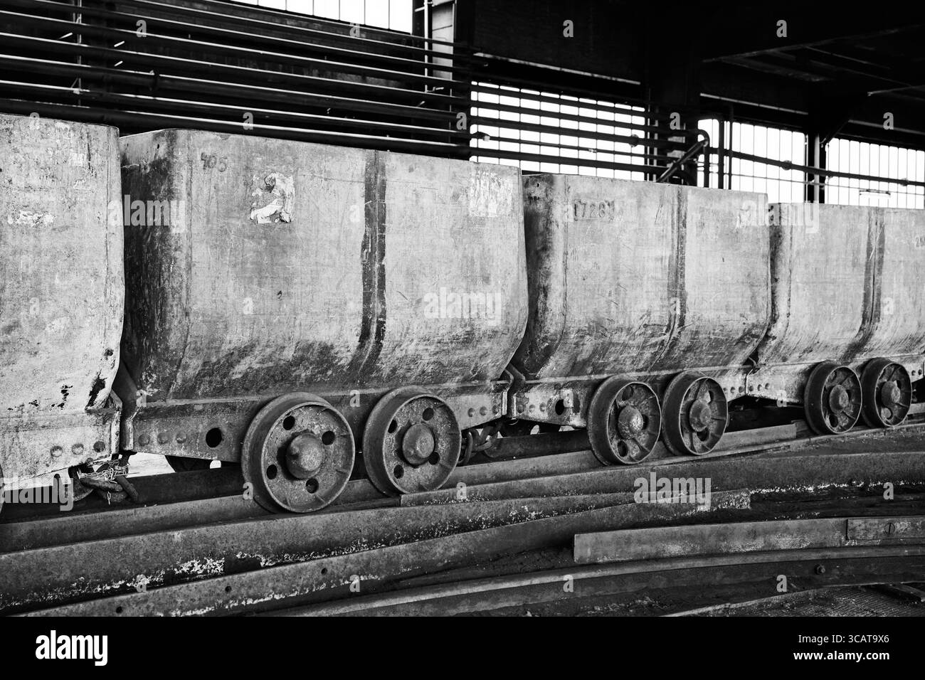 Una fila di carrelli industriali vintage sui binari, con texture intemperie e un'estetica monocromatica. La scena evoca un senso di nostalgia e isto Foto Stock