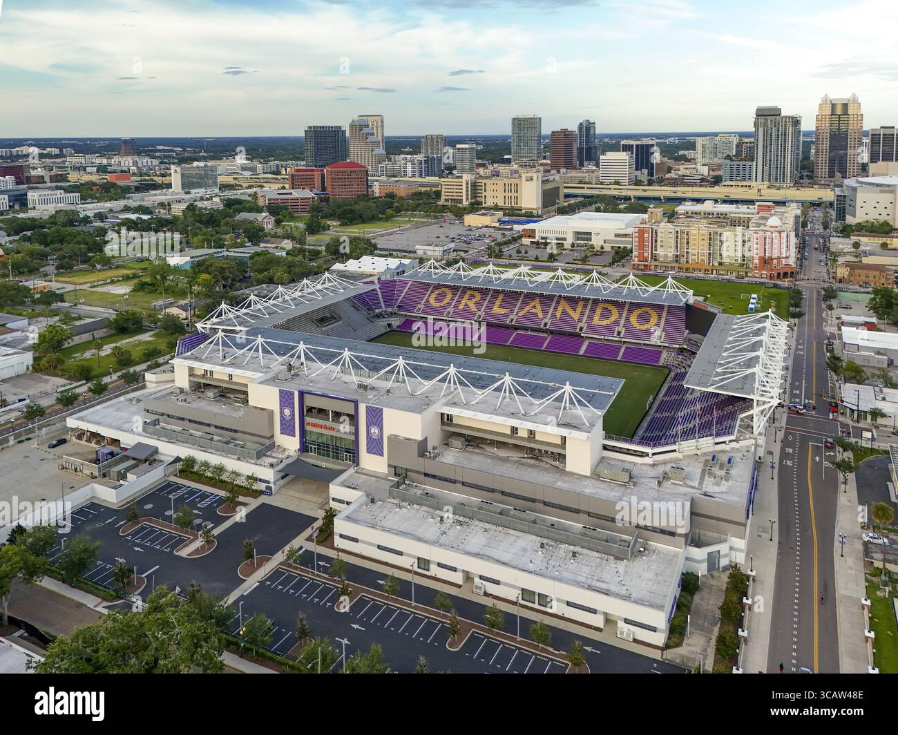 Orlando, Stati Uniti - 21 luglio 2025: Veduta aerea dei posti viola dell'Exploria Stadium e della scritta "ORLANDO" spiccano contro il paesaggio urbano sotto un vasto cielo. Foto Stock