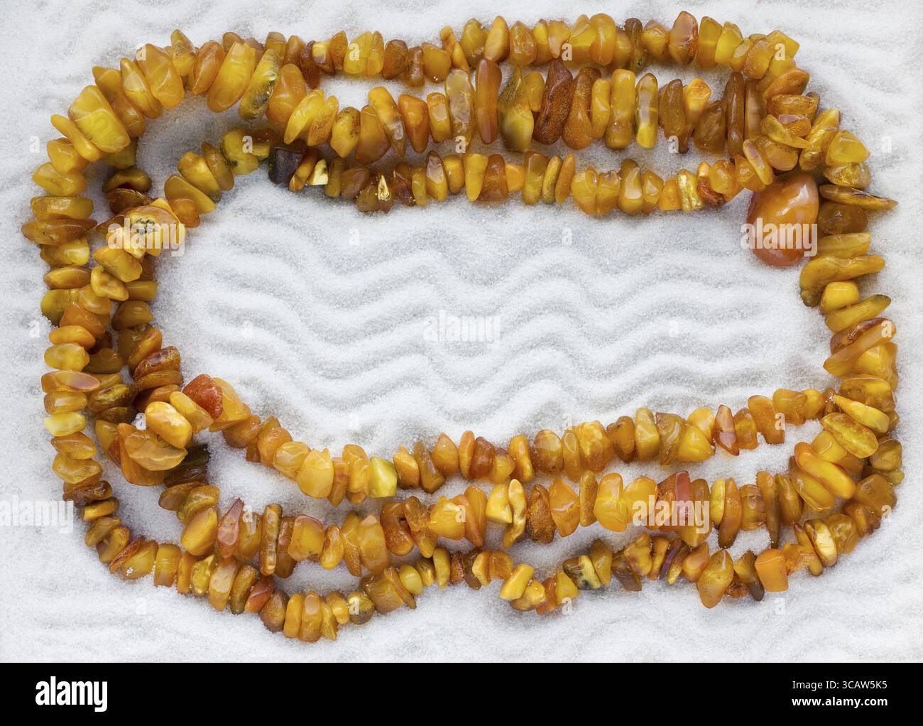 La collana di ambra grezza giace sul puro bianco sabbia di mare. Sfondo di macro Foto Stock