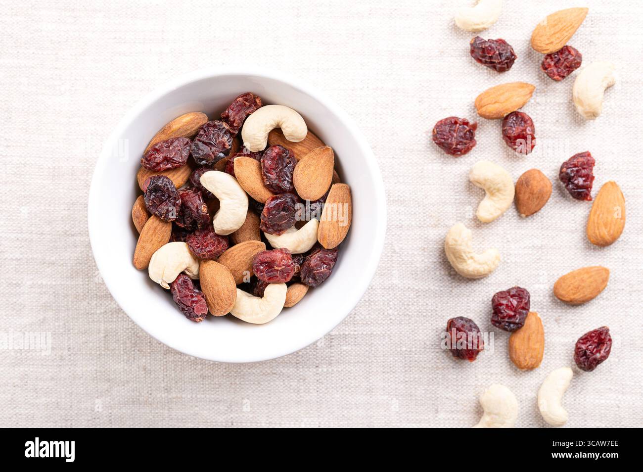 Mix di ciacardi di mandorle di mirtilli rossi, in una ciotola bianca, su lino. Mirtilli rossi secchi, con mandorle crude e anacardi. Spuntini popolari. Foto Stock