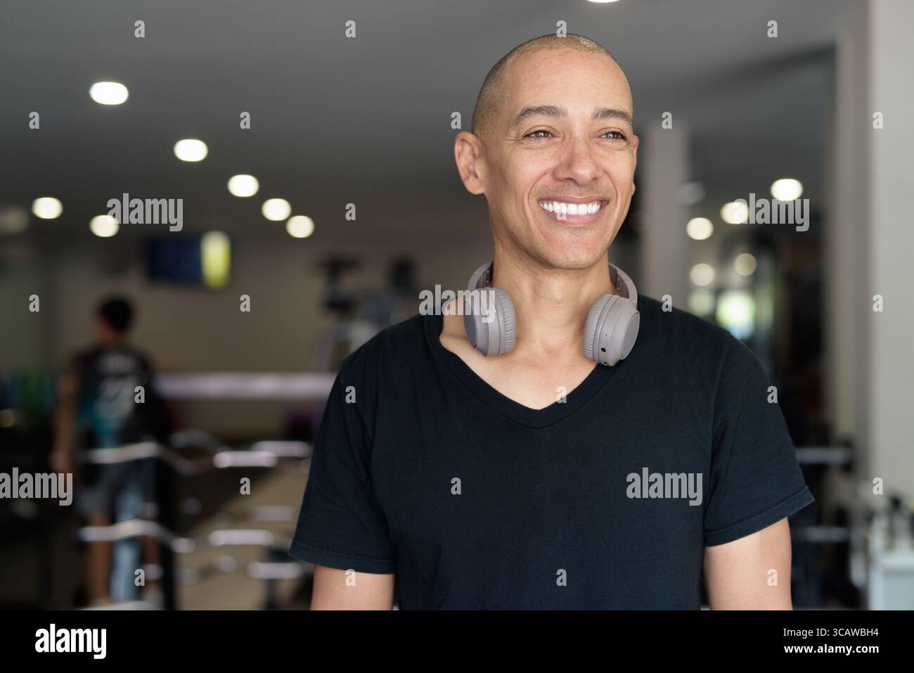 Uomo ispanico calvo che si allena in palestra per il fitness e l'allenamento. Muscoloso maschile che si esercita in casa con sicurezza, indossando camicia nera e cuffie. Healt Foto Stock