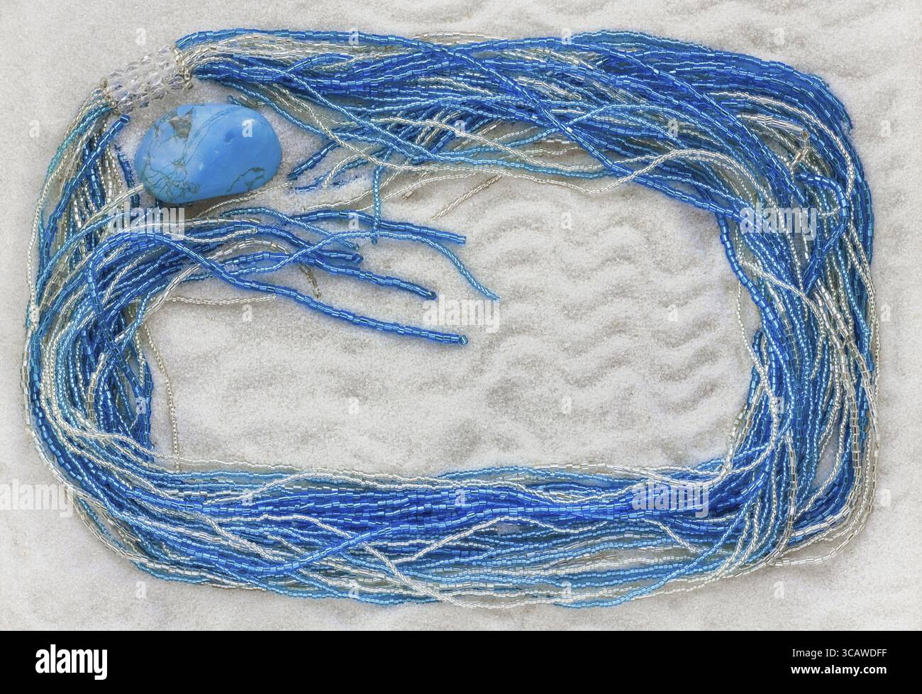 La collana dalle perle di vetro blu e argento giace su sabbia bianca e pura. Sfondo macro Foto Stock