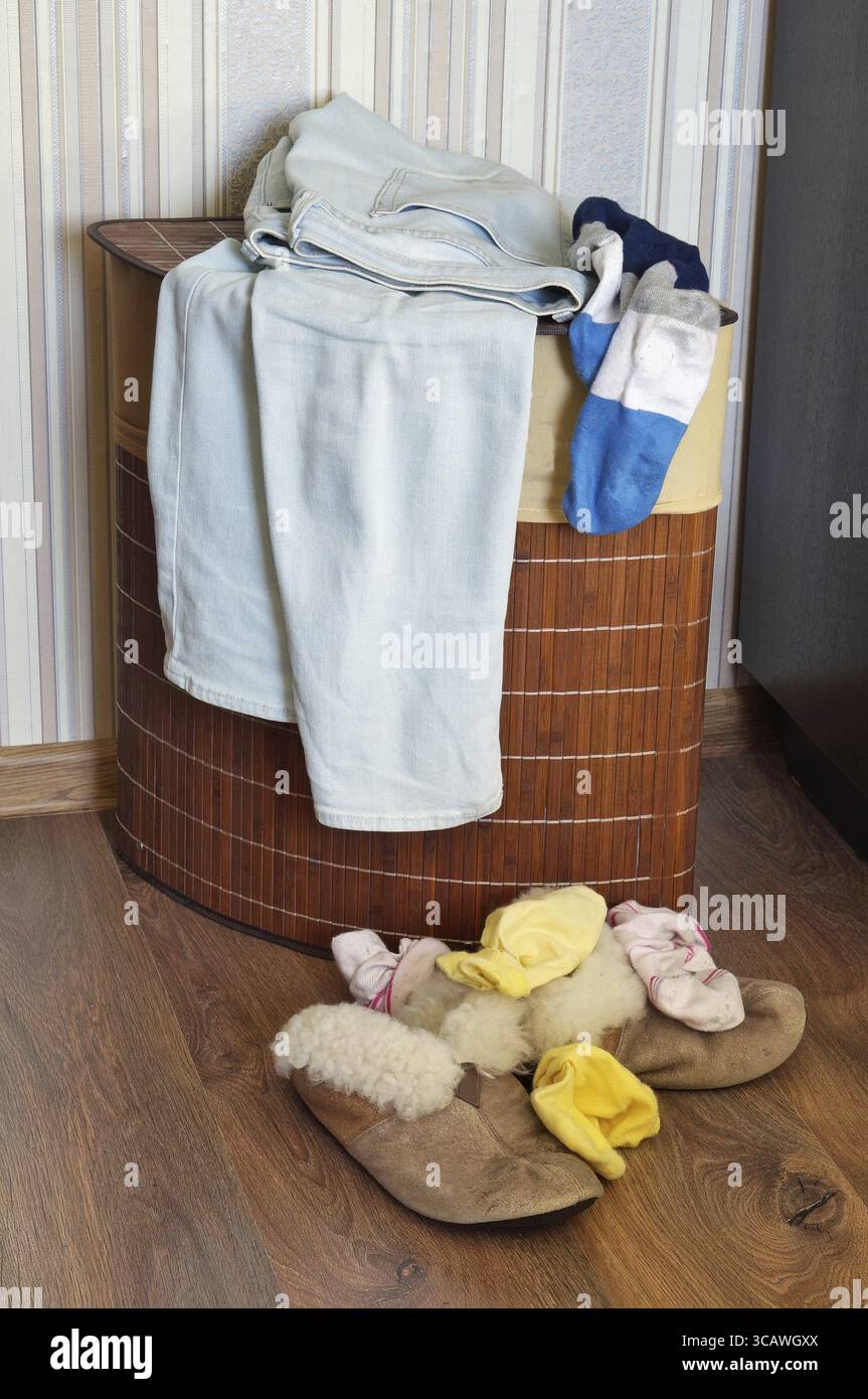 Pantofole e calze da donna in pelliccia vecchia giacciono sul pavimento in legno. Nelle vicinanze c'è un cestino con vestiti sporchi e jeans. Caos nella stanza delle donne¿½ Foto Stock